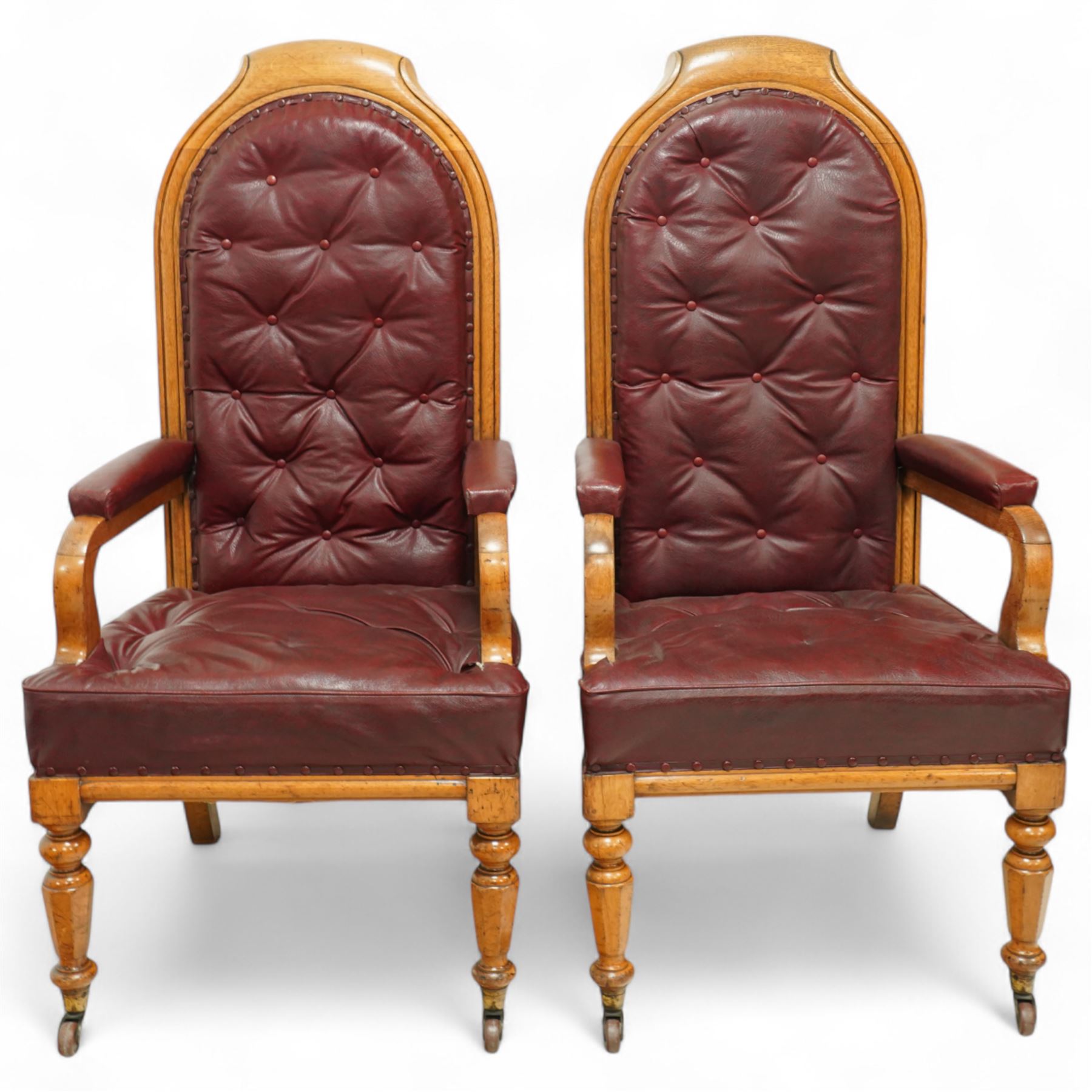 Impressive pair of mid-Victorian oak throne or hall chairs, arched backs on fluted supports with a deep buttoned upholstered panel and upholstered curved arms over fluted seat rails and tapering turned front legs with original brass and brown porcelain castors, and out-swept rear supports