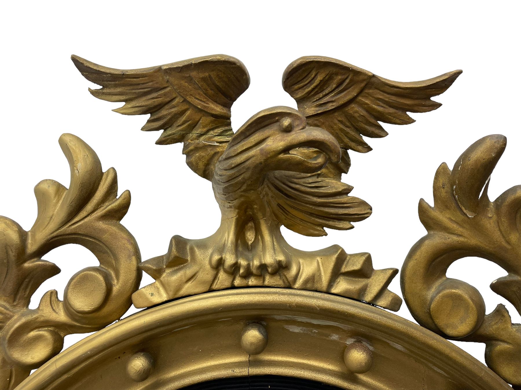 Pair of Regency period giltwood convex wall mirrors, moulded circular frame decorated with spherical mounts surmounted by a carved eagle with spread wings, foliage scroll carved upper and lower brackets, reed moulded and ebonised slip enclosed convex mirror plate 