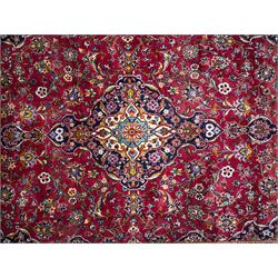 Central Persian Kashan hand-knotted carpet, the madder red field with central lobed medallion in indigo and ivory, enclosing scrolling arabesques and flowerheads, framed by palmette spandrels and an indigo border of rosettes and lotus forms between multiple floral guard stripes, from the region of Kashan