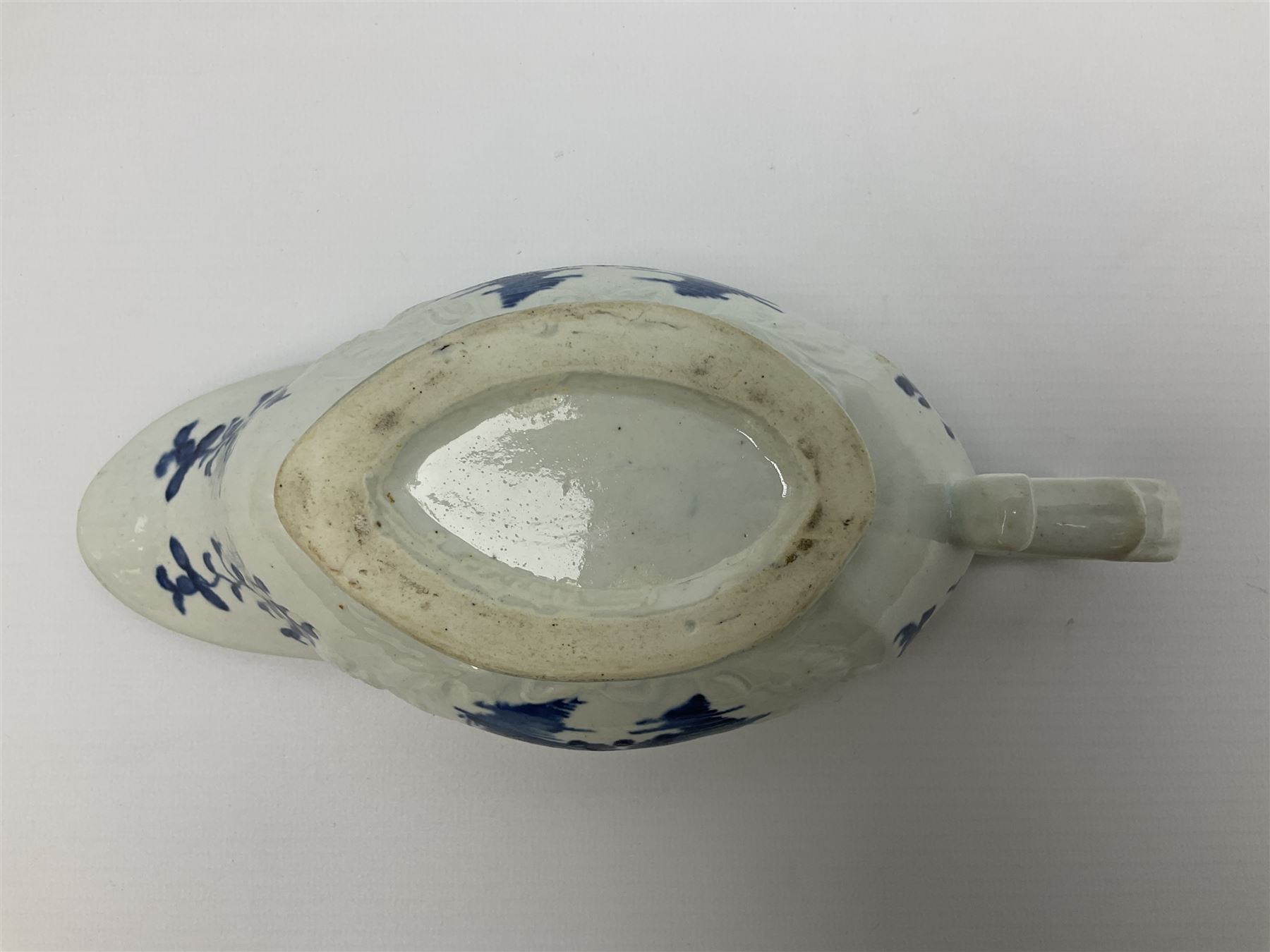 Large 18th century Lowestoft sauce boat, circa 1770, the body decorated with Hughes type floral moulding, and painted in underglaze blue with an Oriental landscape, and foliate sprigs, L23cm