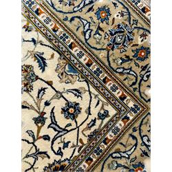 Persian Kashan ivory ground carpet, overall floral design, the field decorated with scrolling and interlaced leafy branches interspersed with palmettes, scrolling border decorated with stylised plant motifs, within floral pattern guard stripes 