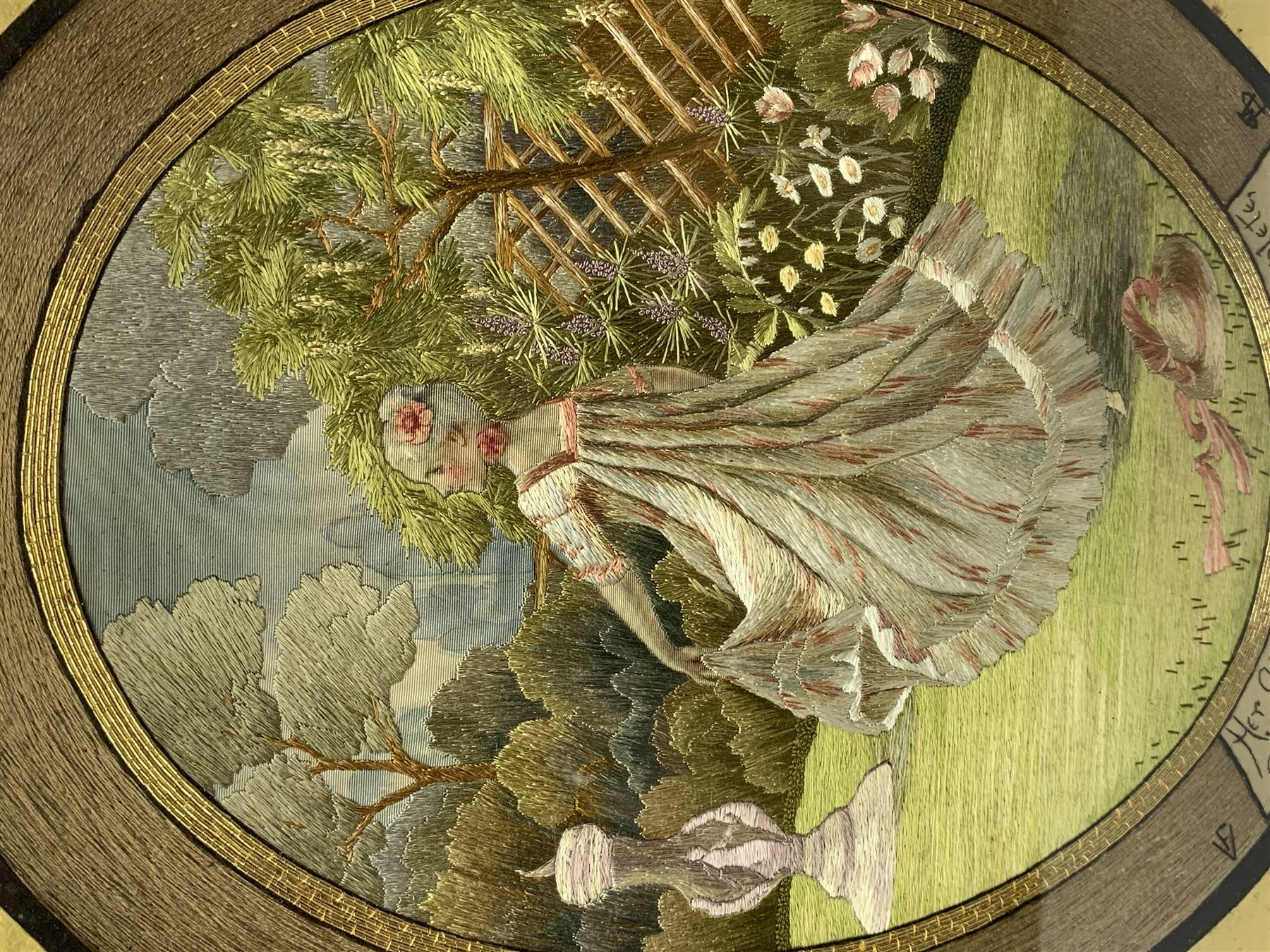 George III silkwork picture, of oval form depicting a female figure in garden setting, within a silkwork border detailed with verse from Robert Burns Bonnie Peg, 'Her air sae sweet, and shape complete, The Queen of Love did never move, Wi' Motion mair enchanting!', and monograms 'FV' and 'SM', in reeded gilt frame and gilt mount, indistinctly inscribed in pencil verso, overall H36cm L30.5cm