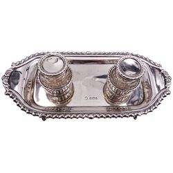 20th century silver desk stand, of shaped oblong form with oblique gadrooned rim, and twin removable glass inkwells with hinged silver covers sat within two pierced circular sections, upon four tapering feet, hallmarked William Hutton & Sons Ltd, Sheffield, date to one inkwell 1923, to other inkwell and stand date letters worn and indistinct, possibly 1911, or 1936, approximate weighable silver 7.58 ozt (236 grams)