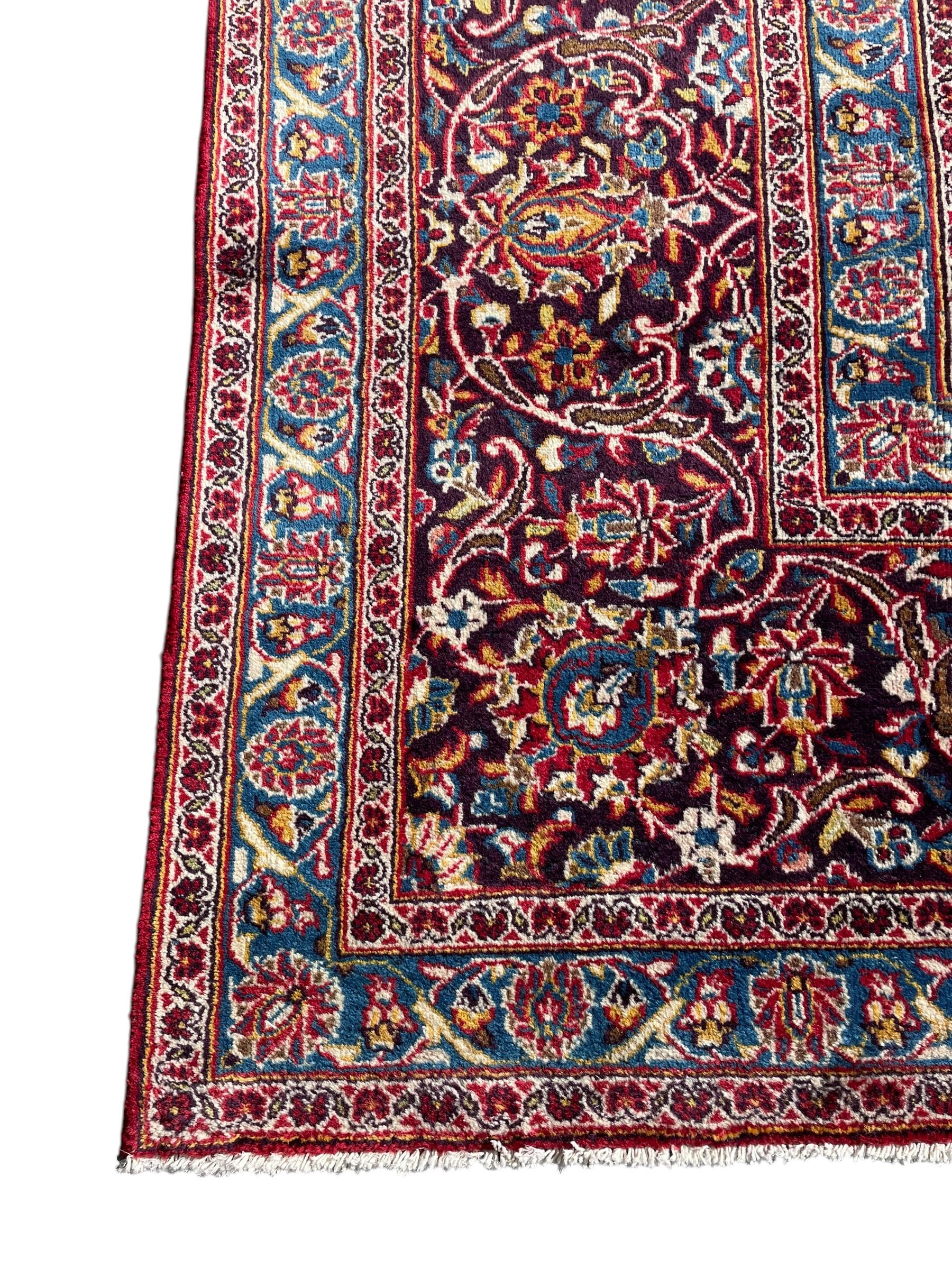 Large Persian Kashan crimson ground carpet, large floral central medallion surrounded by trailing branches decorated with leaves and stylised plant motifs, the main border with scrolling design interspersed with palmettes, within floral pattern guard stripes 