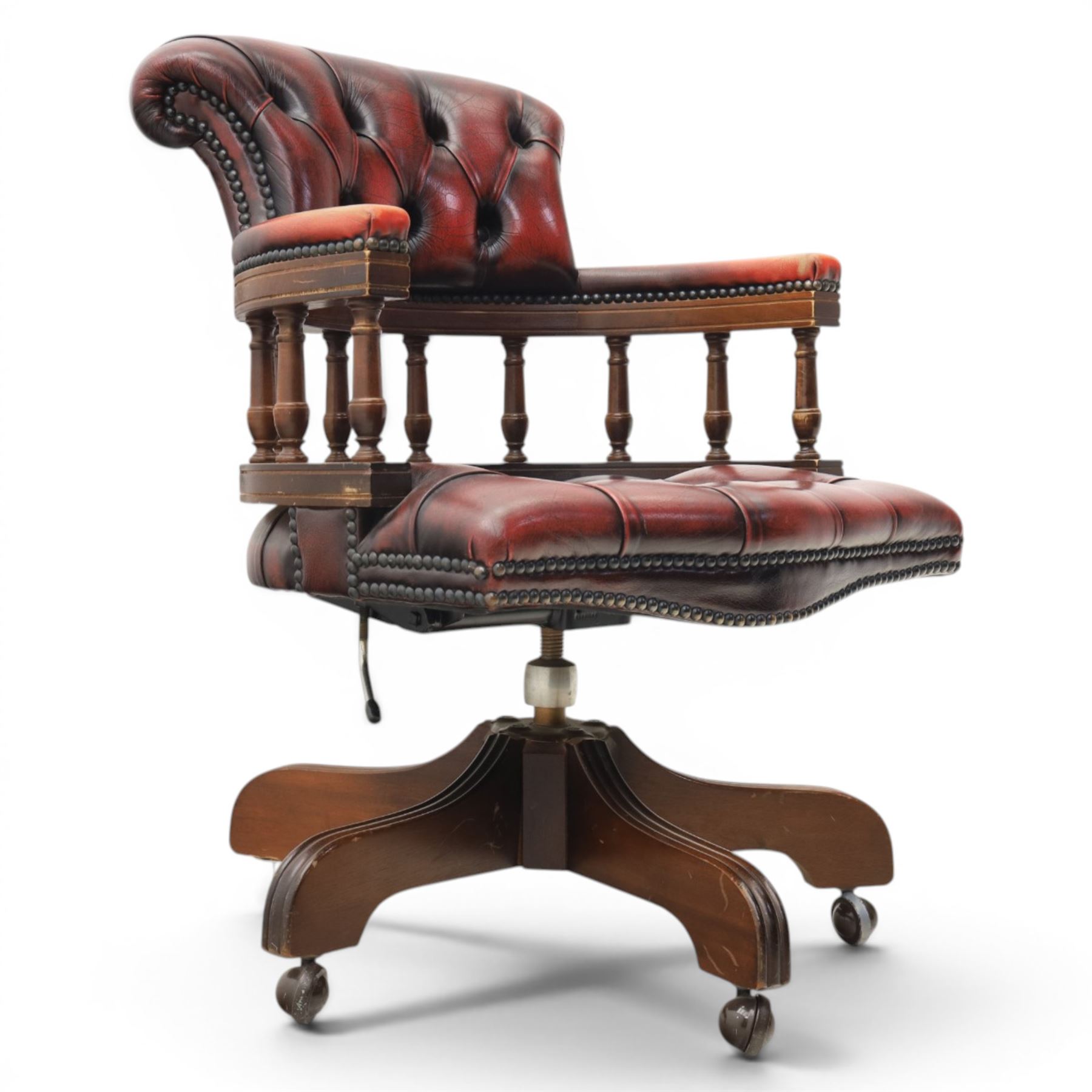 Captains swivel desk chair upholstered in oxblood leather, buttoned back and seat, shaped arm bow raised on turned spindles, five spoke base raised on castors
