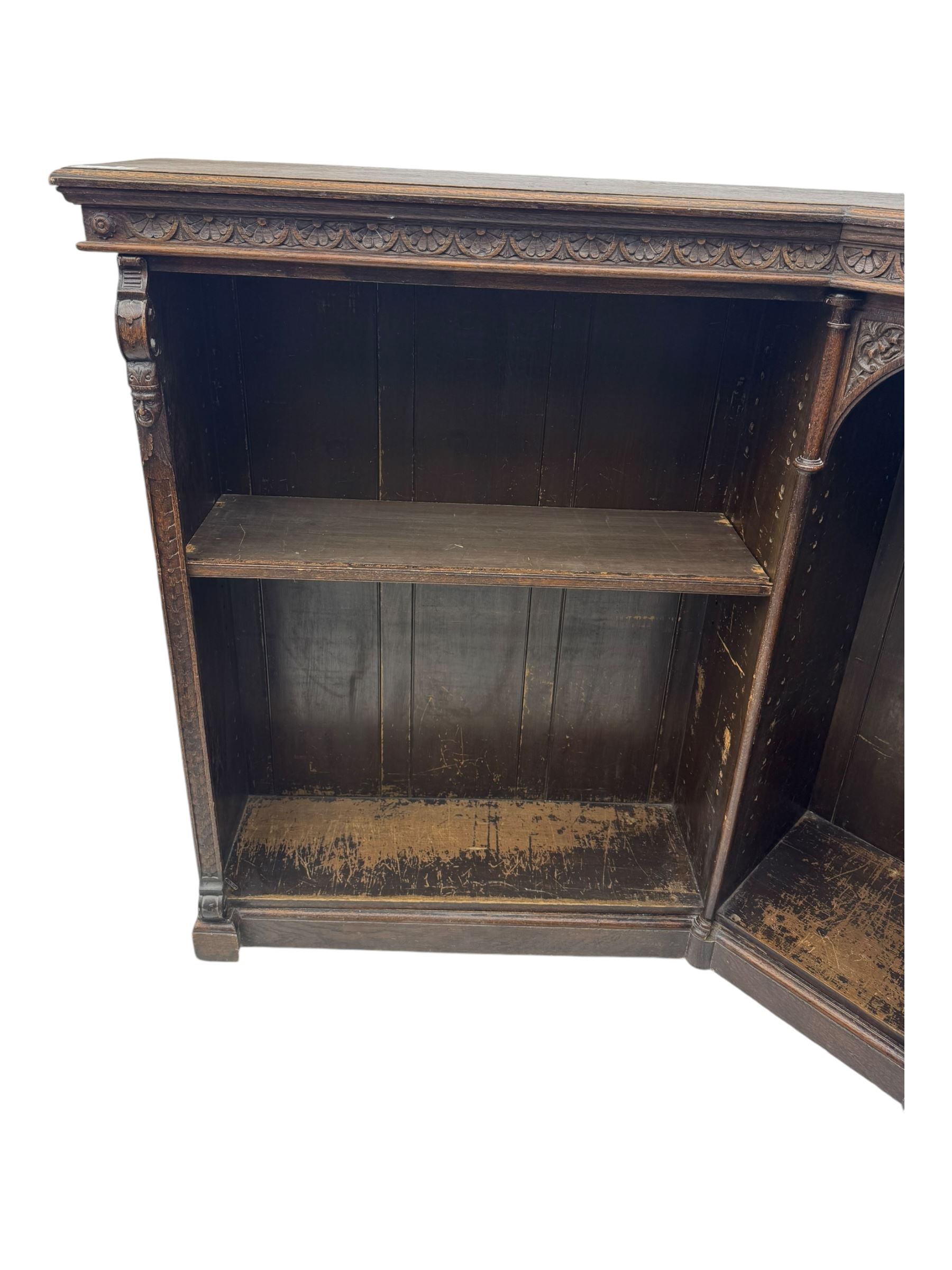Victorian carved oak corner bookcase, L-shaped form, moulded top over lunette carved frieze, decorated with S-scroll and mask carved corbels with trailing acanthus leaves, fitted with adjustable shelves, on moulded plinth base 