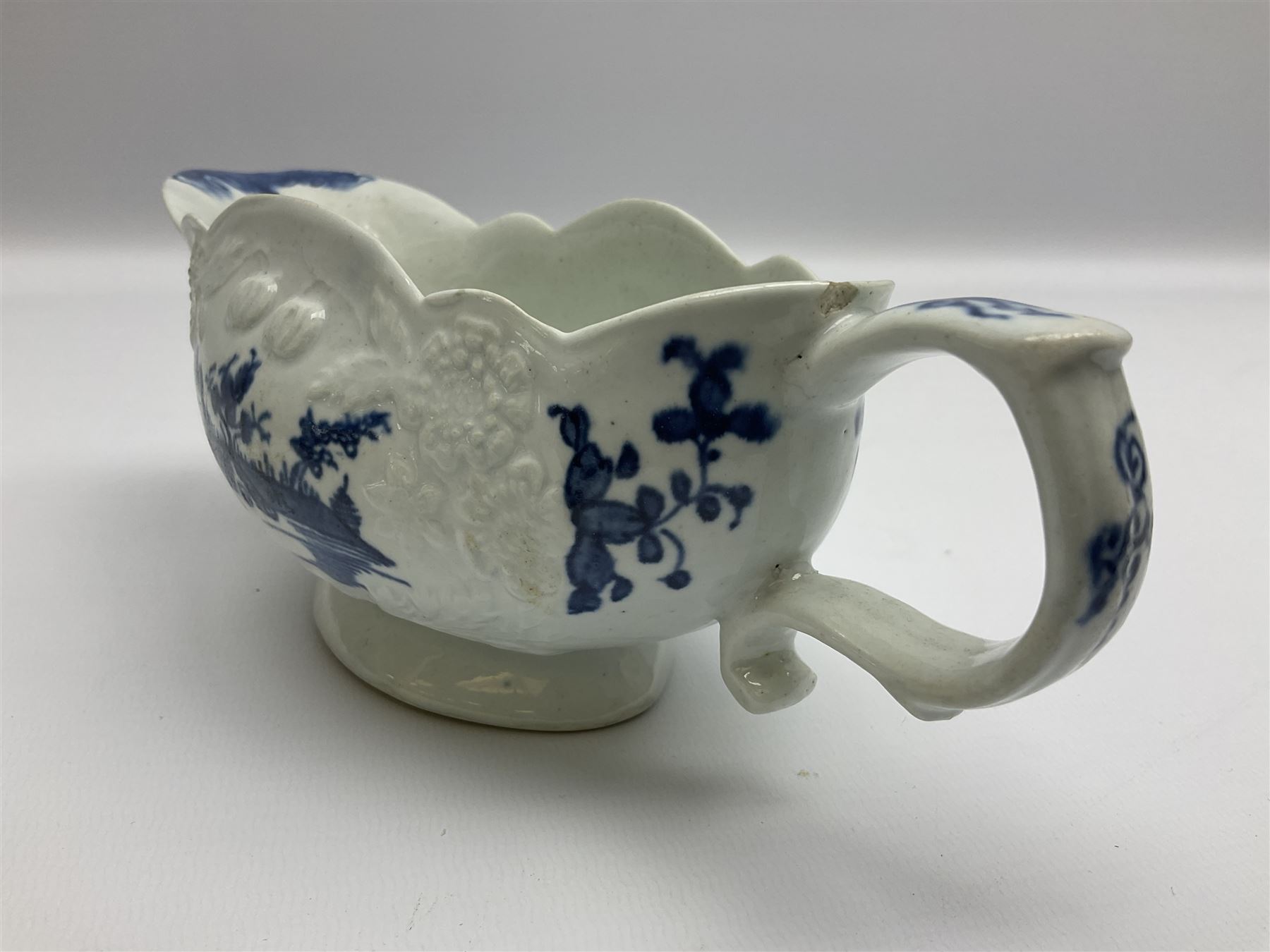 Large 18th century Lowestoft sauce boat, circa 1770, the body decorated with Hughes type floral moulding, and painted in underglaze blue with an Oriental landscape, and foliate sprigs, L23cm