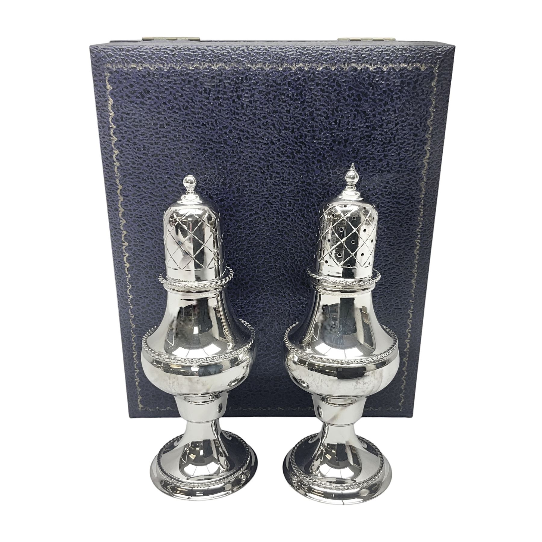Silver plated two piece cruet set, comprising salt shaker and pepper shaker, both of waisted form with engraved rope twist borders, the removable pierced covers each with engraved lattice decoration, upon a circular spreading foot, H13.3cm, contained within velvet lined fitted case