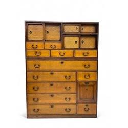 Late Meiji-period Japanese keyaki wood tansu chest, upper section with six sliding woven rattan doors over five drawers, lower section fitted with an asymmetrical arrangement of seven drawers and side cupboard with a hinged door enclosing three additional drawers, iron drop handles to sides