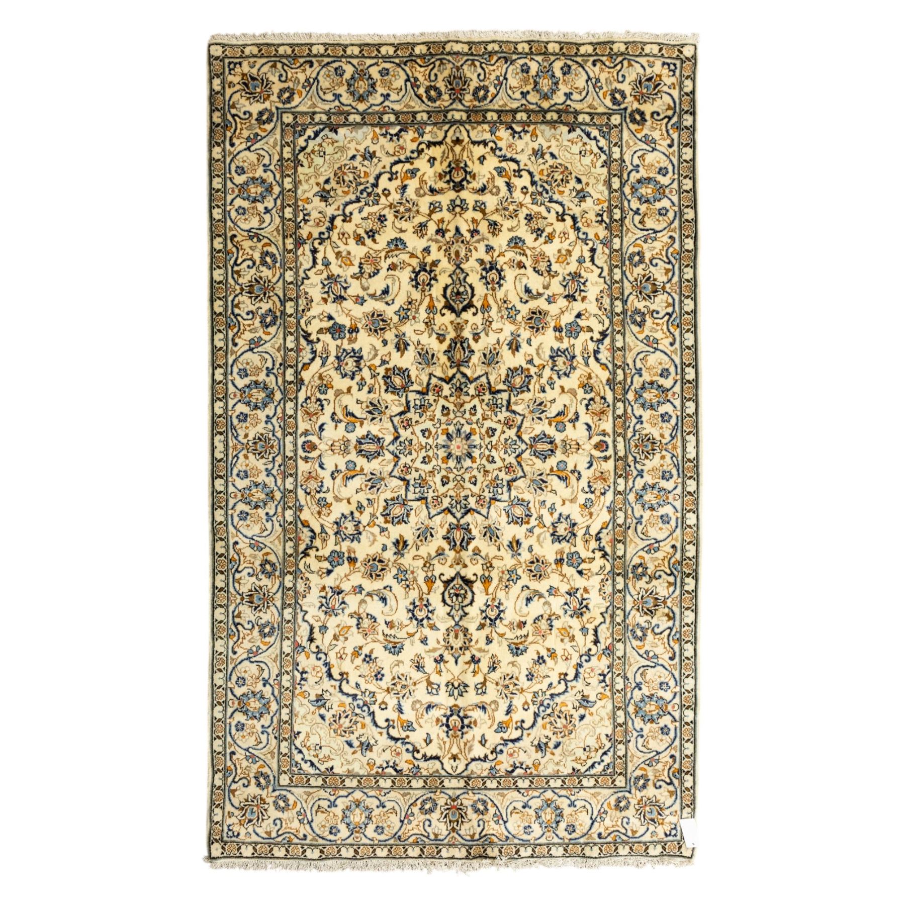 Central Persian Kashan hand-knotted rug, ivory ground, with a small central floral medallion and pendants, the field decorated with fine blue, ochre and beige scrolling vines, flowerheads and palmettes, within an ivory border of repeating floral sprays and meandering vines, flanked by narrow guard stripes, with cotton fringes