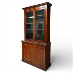Large Edwardian walnut and satinwood enclosed bookcase-on-cupboard, projecting cornice over two glazed doors with satinwood and ebony banding and stringing enclosing three adjustable shelves, over two panelled doors enclosing two drawers above shelf, on skirted base