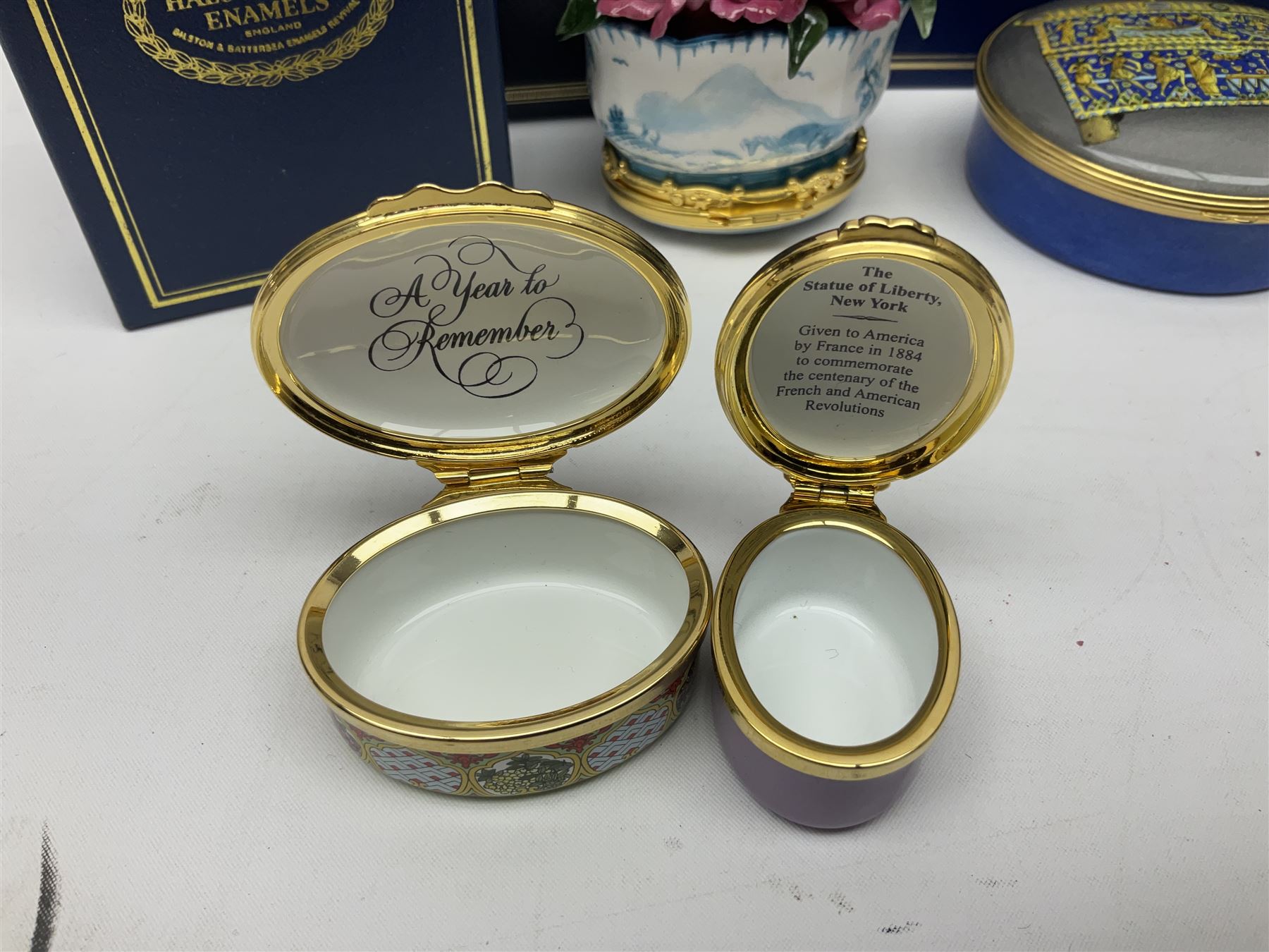 Halcyon Days bonbonniere, modelled as pink roses in a planter painted with a blue and white Japanese scene, together with five Halcyon Days enamel boxes, one a larger example depicting 'The Becket Casket' and four smaller boxes, including The 1993 Easter Egg, Happy Birthday and Statue of Liberty examples, all boxed, Becket Casket D8cm