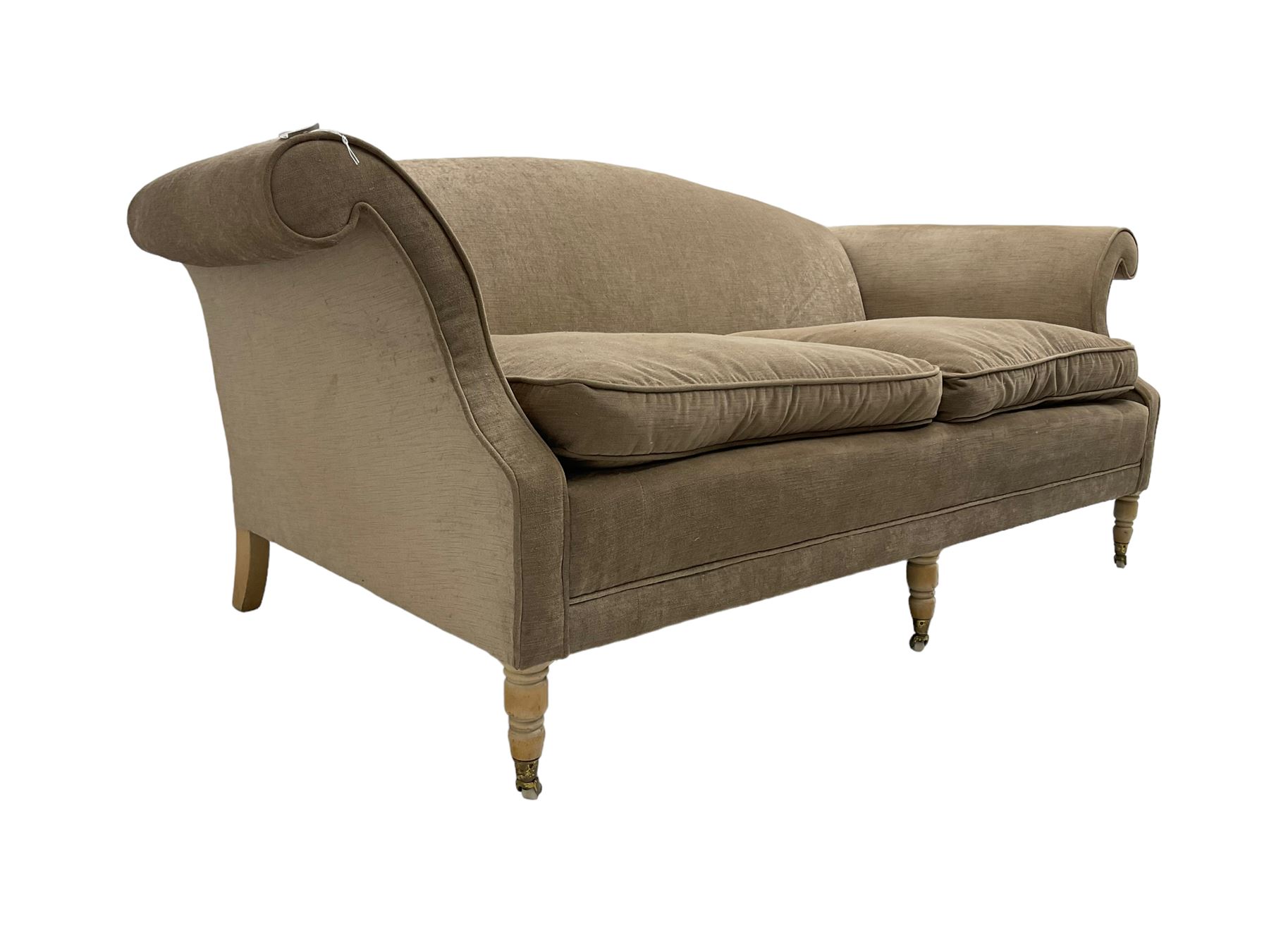 Traditional three seat sofa, curved back over scrolled arms, upholstered in crushed beige fabric with matching loose cushions, on turned front supports with brass and ceramic castors, together with matching footstool