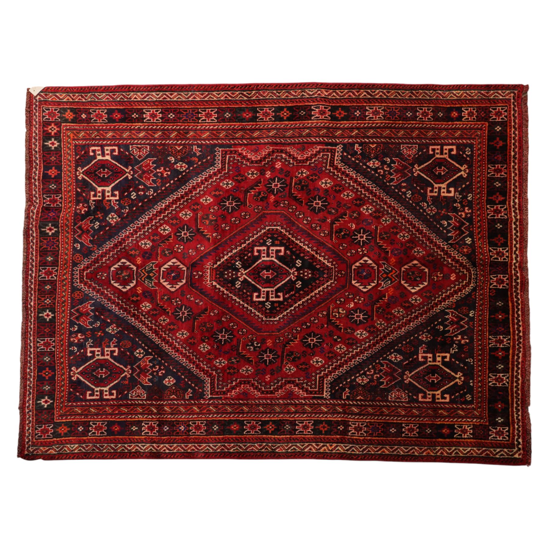 South West Persian Qashqai hand-knotted rug, madder red field with a large stepped diamond medallion with scattered geometric devices and indigo spandrels filled with geometric motifs, framed by multiple narrow guard borders and broad main border, wool fringe ends 