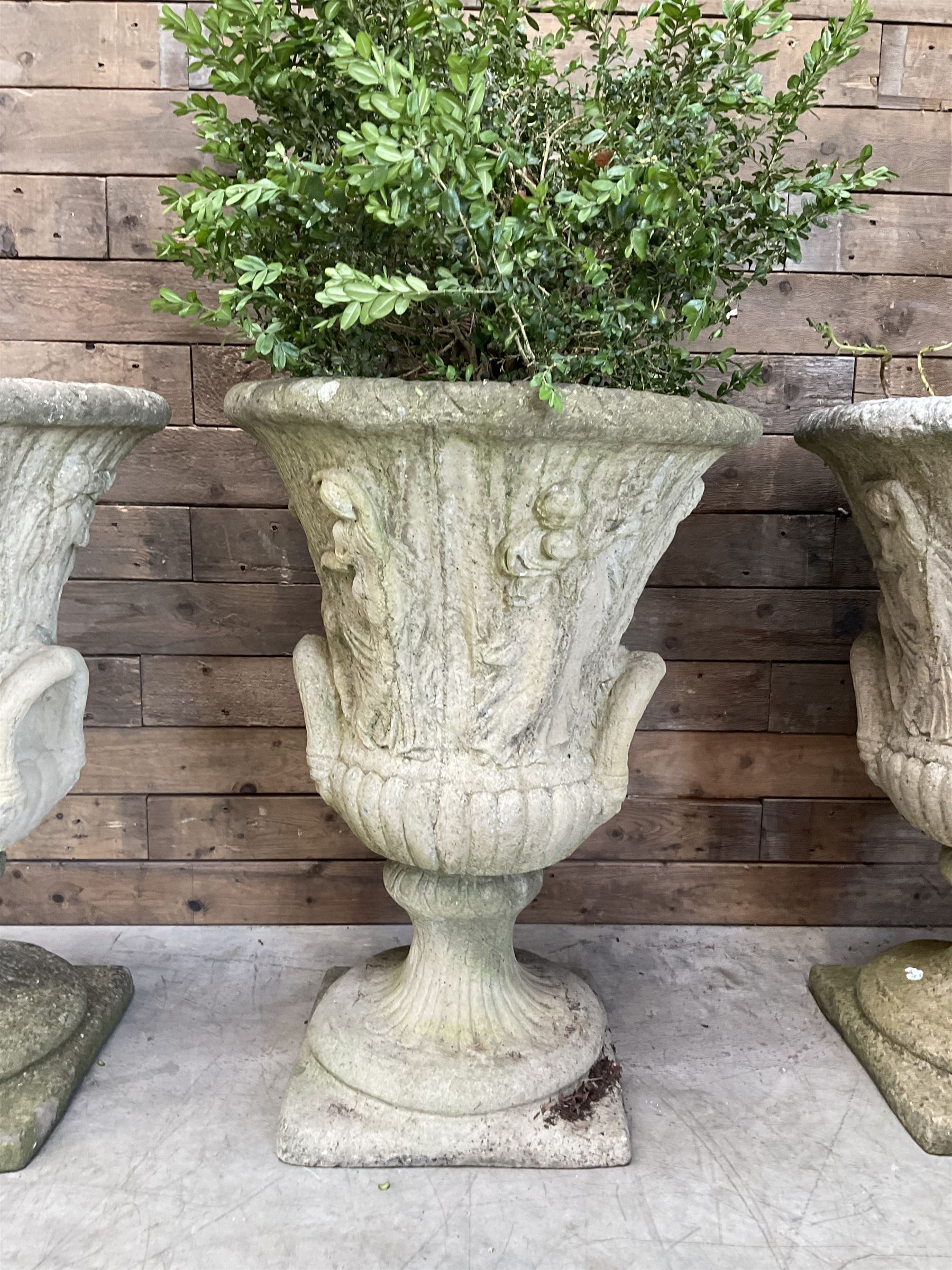 Set of four Victorian design cast stone Grecian urns, tapering form cast with figures and handles, square plinth bases