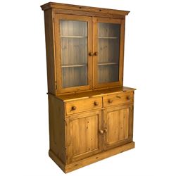 Large pine bookcase on cupboard, the upper section enclosed by two glazed door, the lower section fitted with two drawers and double cupboard, on plinth base