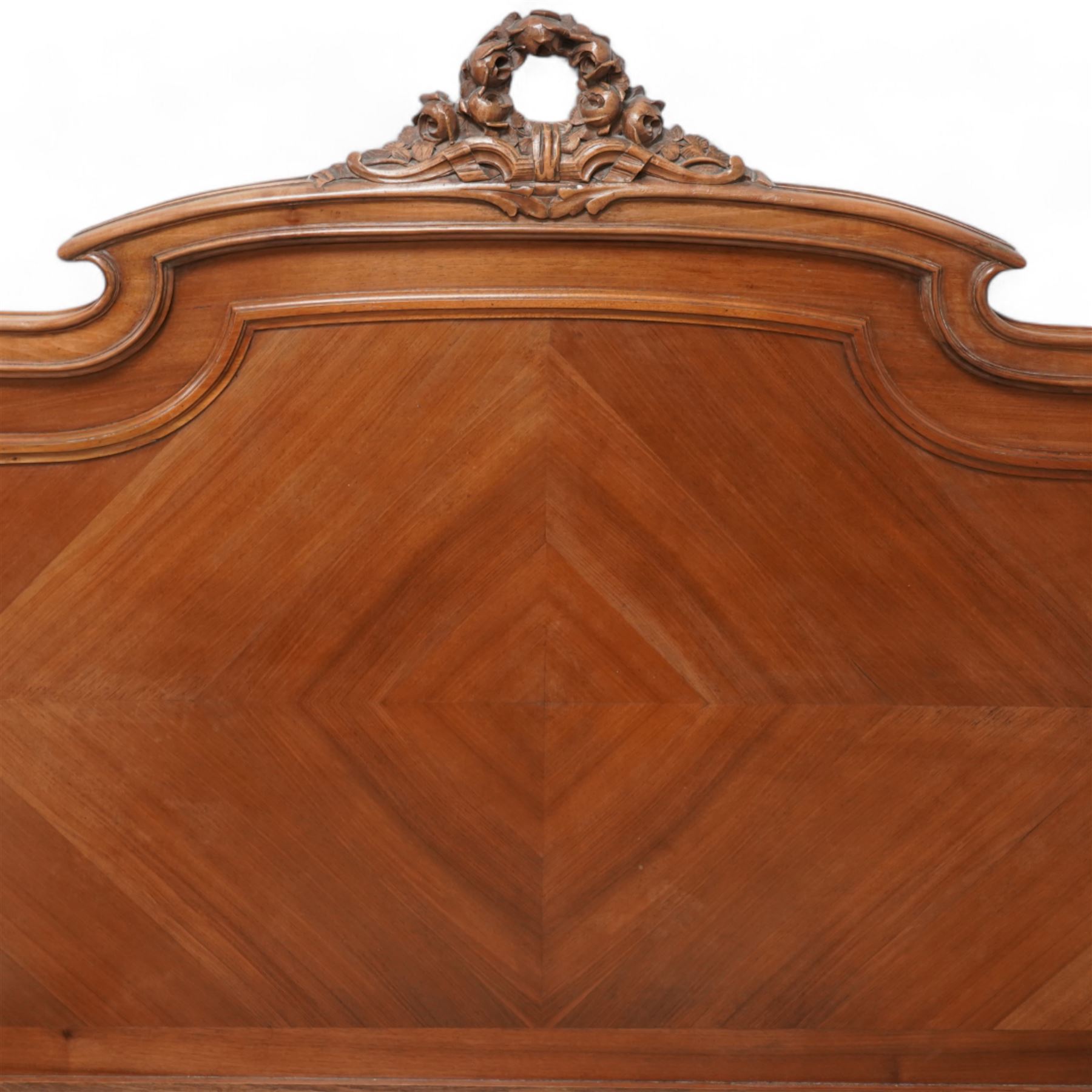 20th century French walnut 4' 6'' double bedstead, the headboard with flower head wreath pediment flanked by carved pineapple finials, reed and ribbon carved corner uprights, quarter-matched veneers, on turned feet, together with upholstered bed base