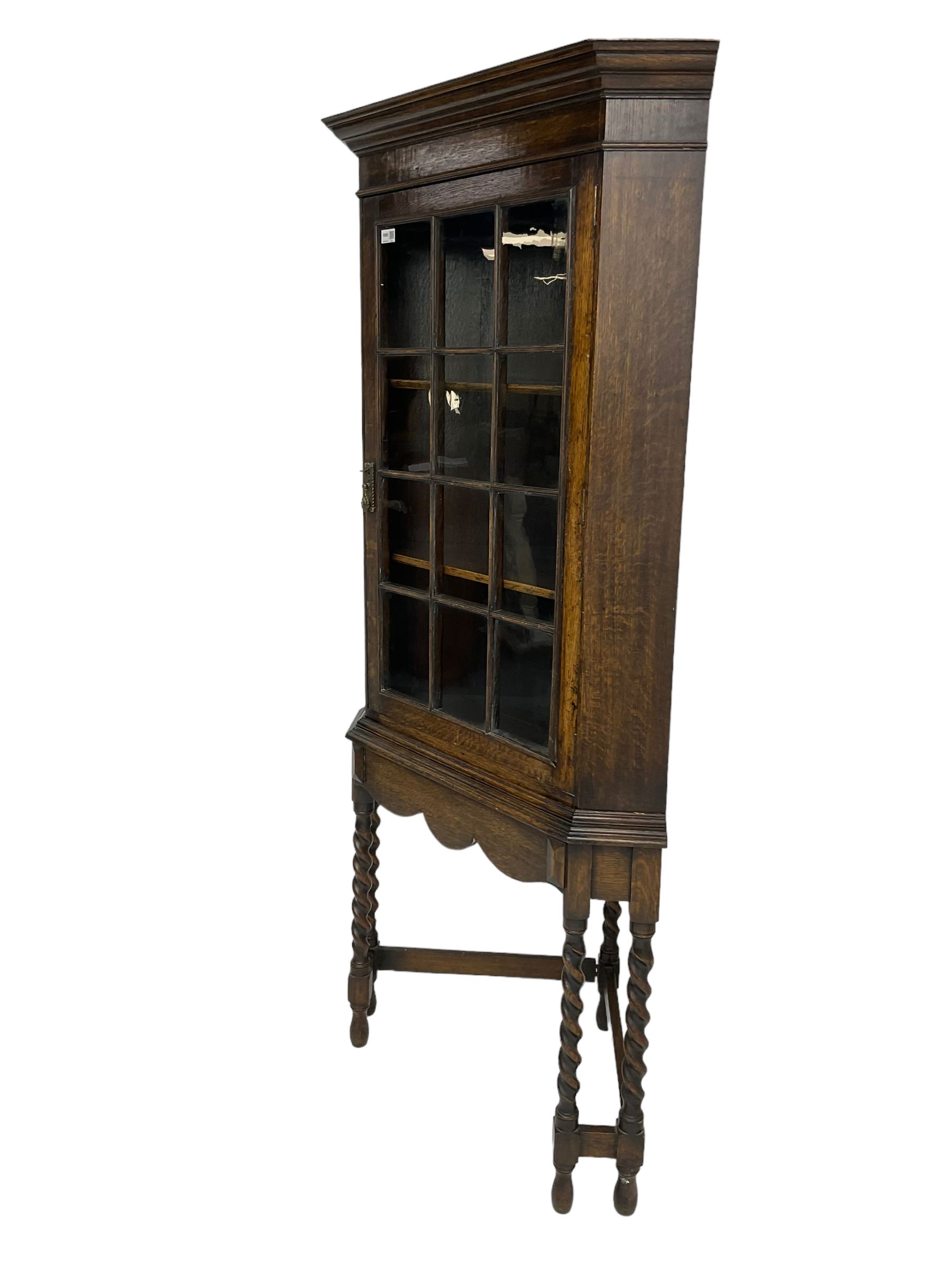 Early to mid-20th century oak corner display cabinet, projecting cornice over astragal glazed door, on spiral turned supports joined by stretchers