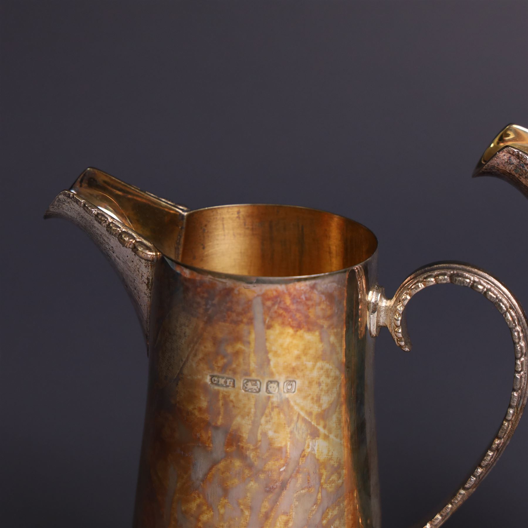 Two graduating silver milk jugs, each of tapering cylindrical form, with engraved central cartouche to body and upon three paw feet, hallmarked Christopher Nigel Lawrence, London 1988, tallest H13cm