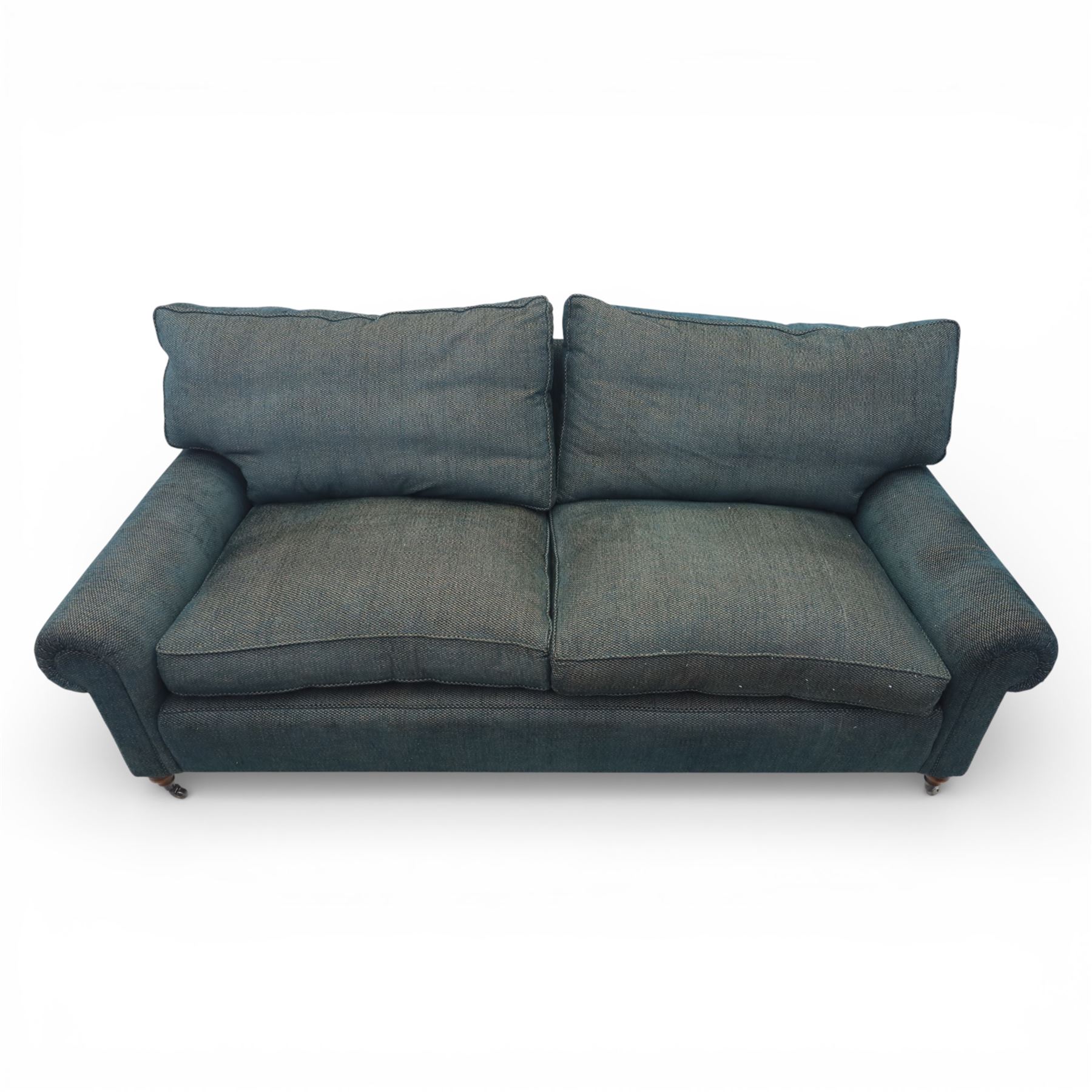 Late 20th century three seat sofa upholstered in green fabric, with gently rounded scroll arms, loose seat and back cushions, raised on turned wooden legs with castors, rear splayed legs