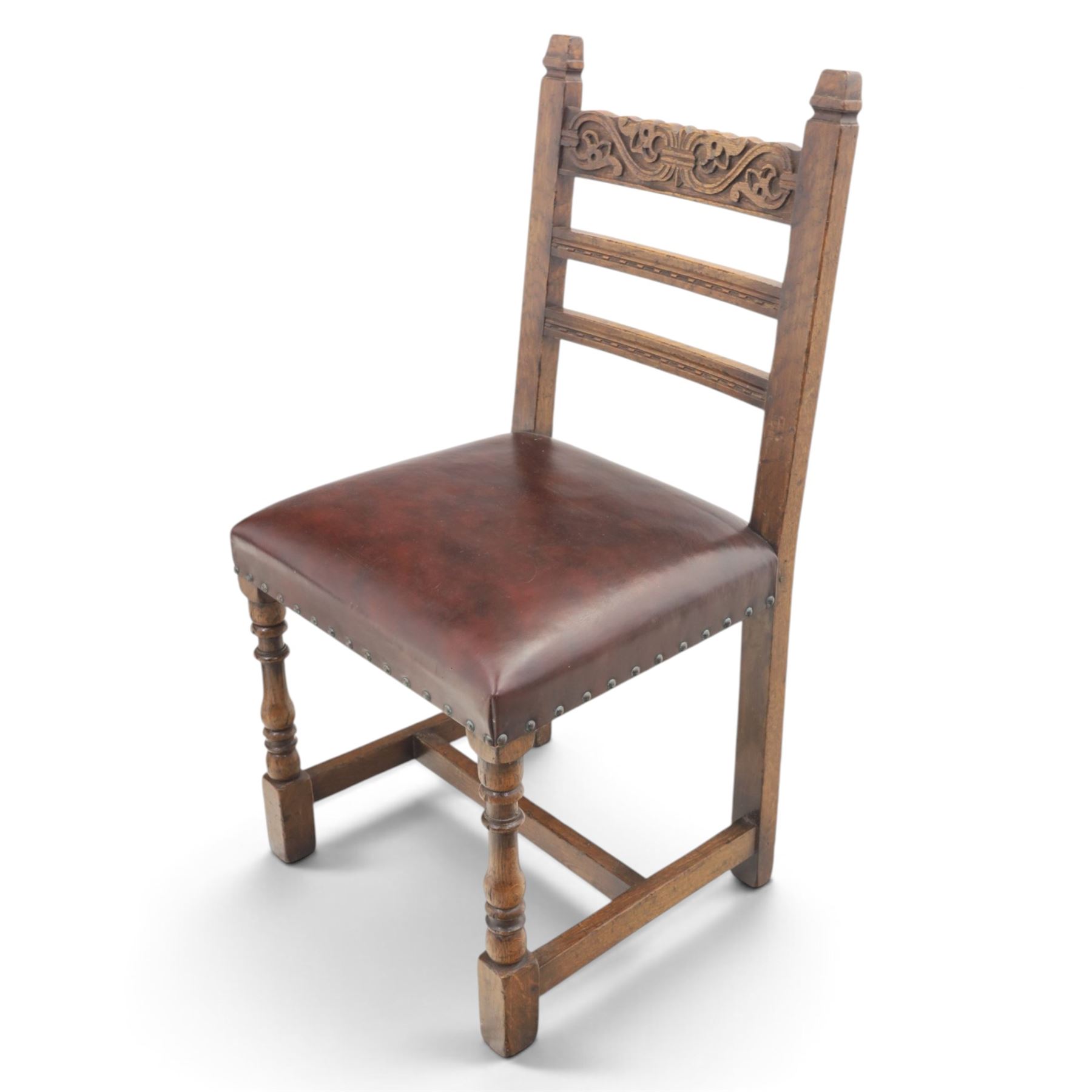 Craftsman made set of four solid oak dining chairs with leather seats, with carved cresting rail, on red leather seats with studded trim, raised on block and turn supports united by H-stretcher