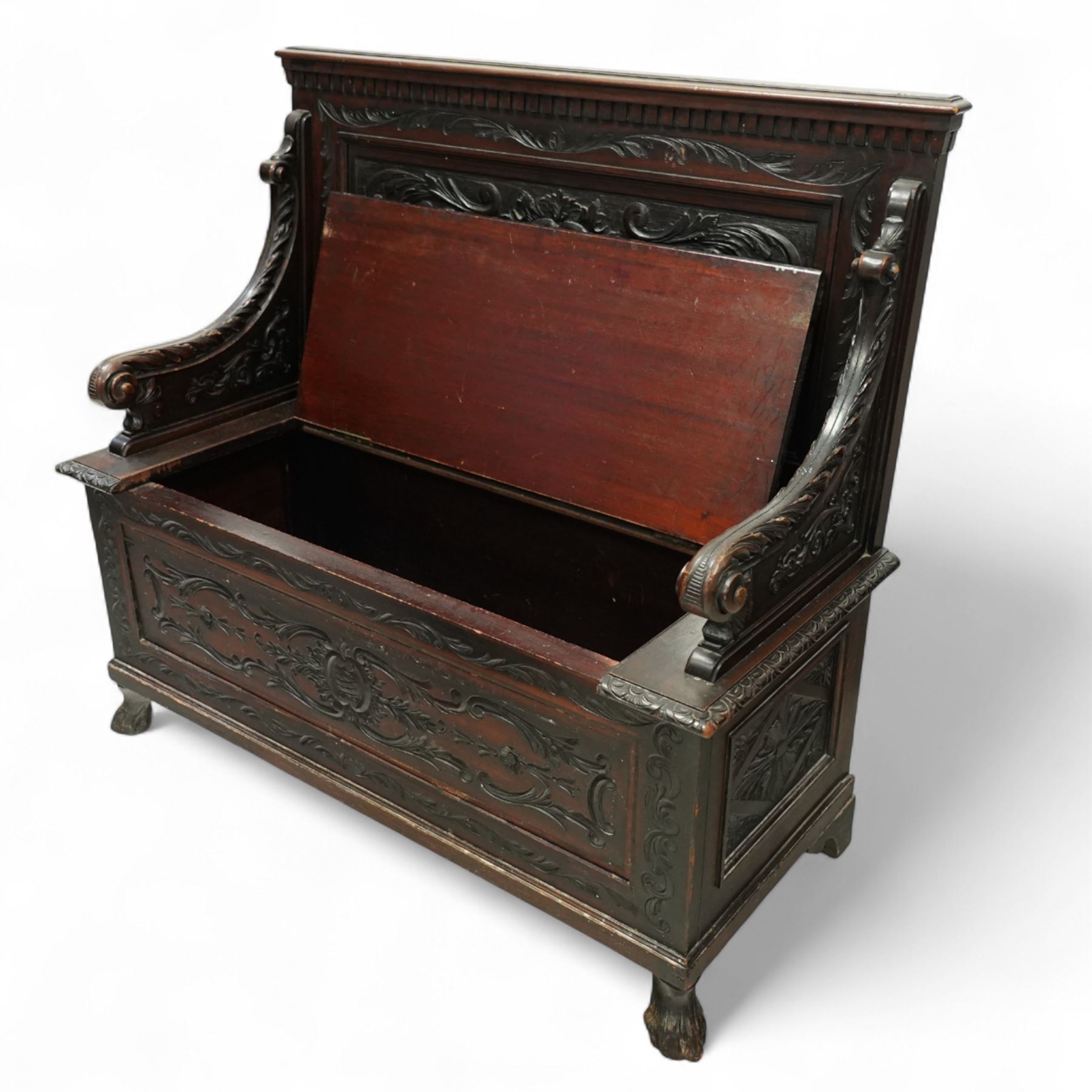 Late Victorian carved oak hall bench, the panelled back deeply carved with scrolling acanthus and central cartouche, hinged seat with foliate and shell motifs, scroll carved arm supports, on short cabriole front legs