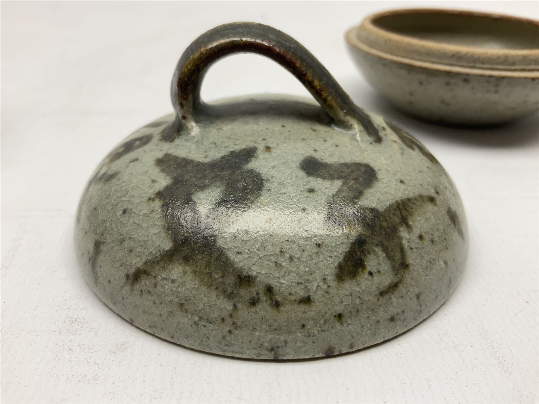 Janet Leach (American, 1918-1997) for Leach Pottery; speckled studio pottery vase of shouldered ovoid form with speckled brown decoration and trailing green and brown glaze upon beige and brown ground, with impressed J.L. monogram and Leach Pottery mark beneath, together with a Jeremy Leach blue speckled lidded circular dish with loop handle, impressed J.L, tallest H11cm