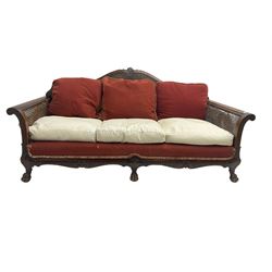 Early 20th century bergère three seat settee, shaped shell carved cresting rail, double caned back and sides, scrolled upright arms and shaped apron carved with shell and foliage, on hairy paw carved feet