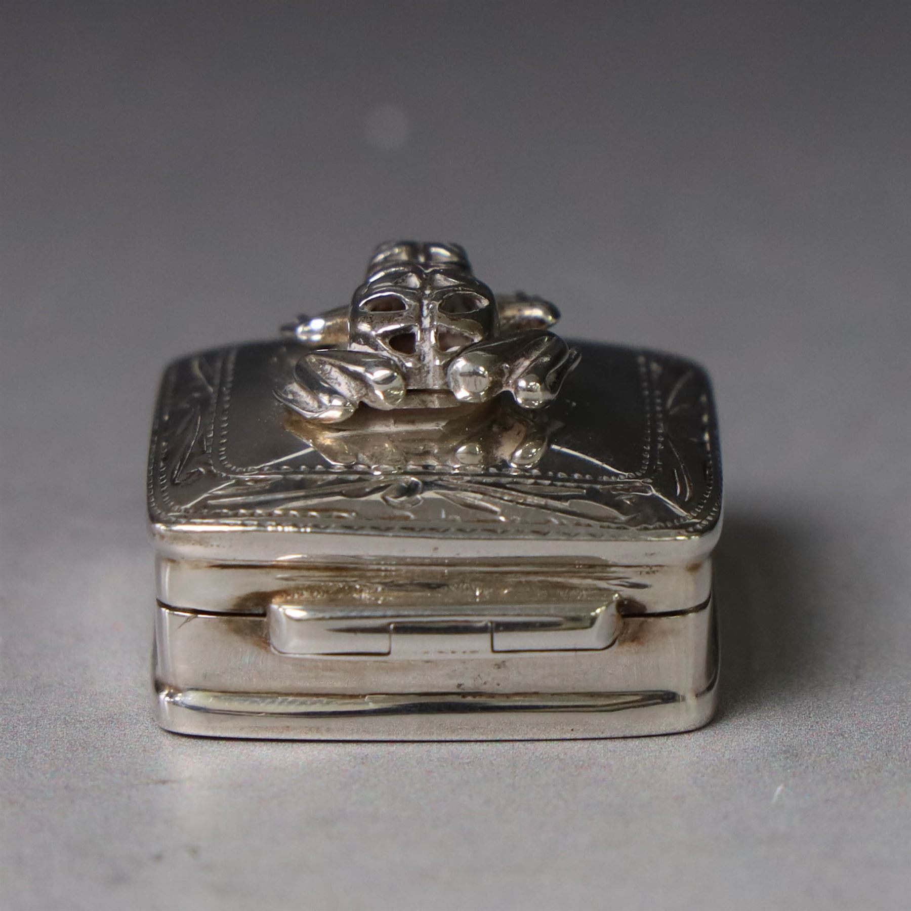 Modern silver pill box, of square form, the hinged cover surmounted with figure of a frog within a engraved scroll edge, hallmarked hallmarked Martin Gerald & Sid Adler, London 2000, W3cm