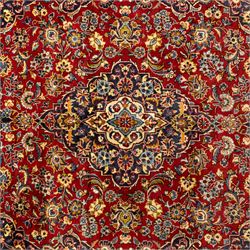 Central Persian Kashan hand-knotted carpet, crimson red central field with central floral medallion with floral vine-work and palmettes, within dense floral spandrels and a wide navy blue border decorated with continuous foliate motifs and multiple guard borders, with cotton fringe ends  