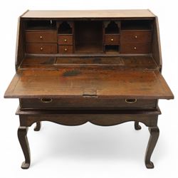 Early 18th century George I oak bureau on original stand, the fall front enclosing an arrangement of correspondence drawers and pigeonholes over central well, fitted with single long drawer below, the shaped apron over cabriole supports with pad feet