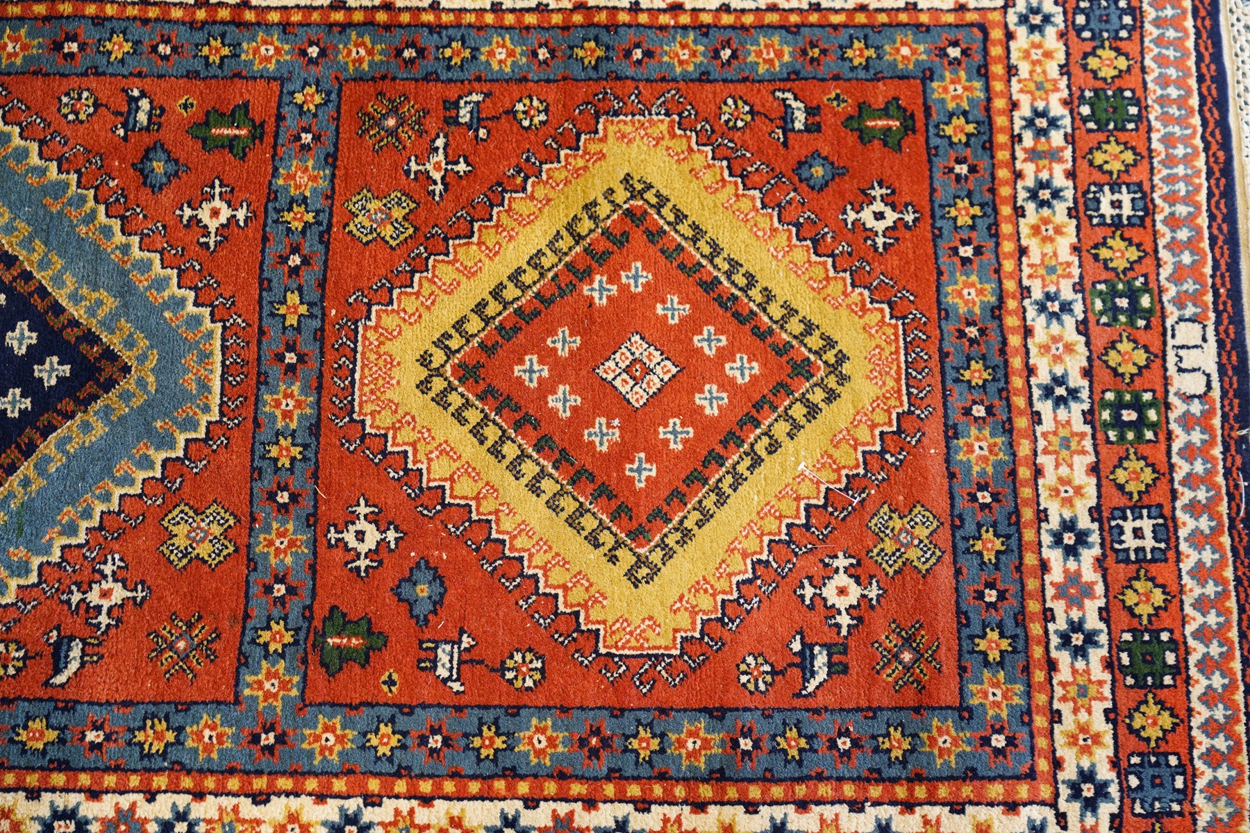 Caucasian Kazak vermillion ground rug, the sectioned field decorated with three geometric lozenge medallions surrounded by stylised plant and animal motifs, the multiple guard bands with repeating geometric design
