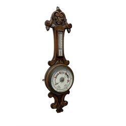 English - Edwardian aneroid barometer in a carved scroll work oak case, with a mercury box thermometer recording room temperature in degrees Fahrenheit and Celsius, circular  porcelain register written in gothic script with weather predictions and barometric air pressure from 26 to 31 inches, steel indicating hand and brass recording hand.