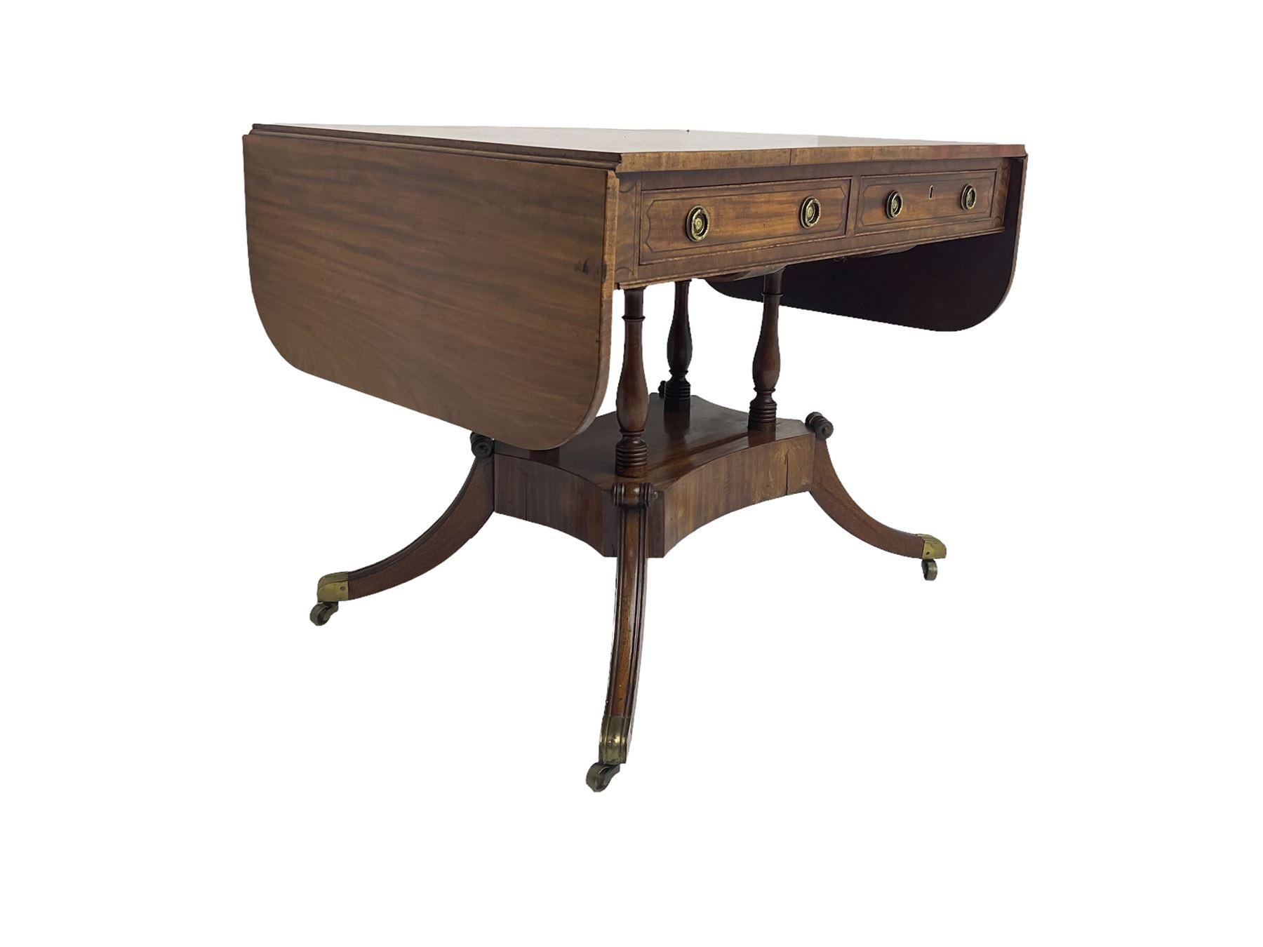 Regency period mahogany drop-leaf sofa table, rectangular top fitted with two cockbeaded drawers with ebony stringing, raised on turned columns united by quadrupod base, the sabre supports terminating in brass cups and castors