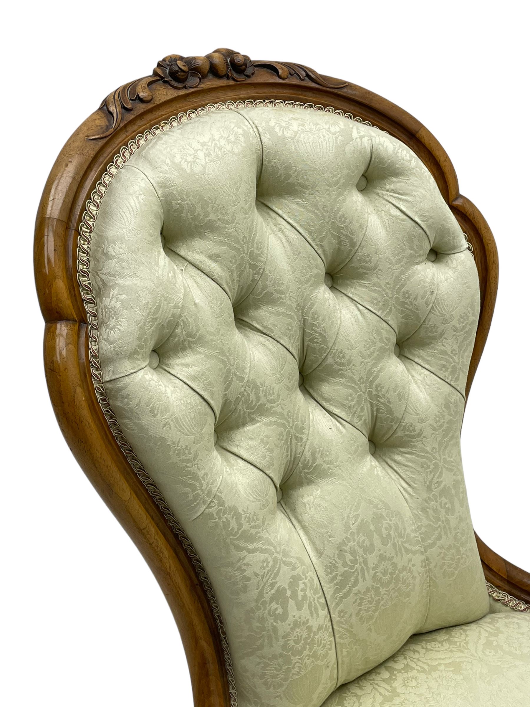 Victorian walnut framed nursing chair, the cresting rail decorated with carved applied flower heads and acanthus leaves, shaped back and sprung seat upholstered in buttoned ivory damask fabric, serpentine front over cartouche carved cabriole supports with ceramic castors (W57cm H92cm); with matched footstool, circular top over shaped moulded apron, on floral carved cabriole feet (W34cm) 