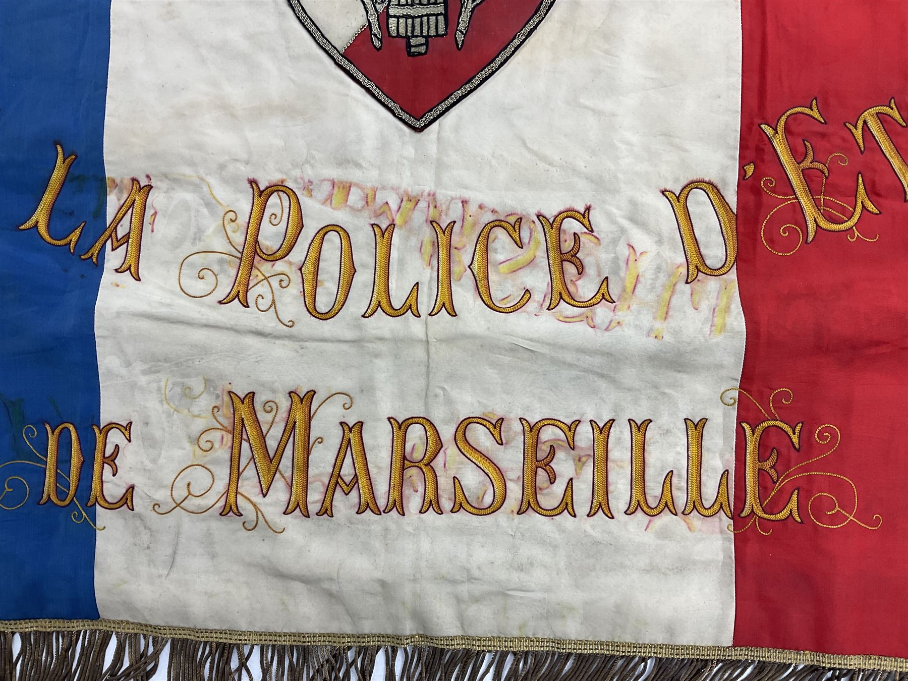 French State Police banner as the tricolor flag embroidered with coloured and metallic thread 'Societe De Secours Mutuels Un Pour Tous Tous Pour Un De La Police D'Eteat De Marseille' to one side; plain flag verso; tassels to three sides 100 x 113cm