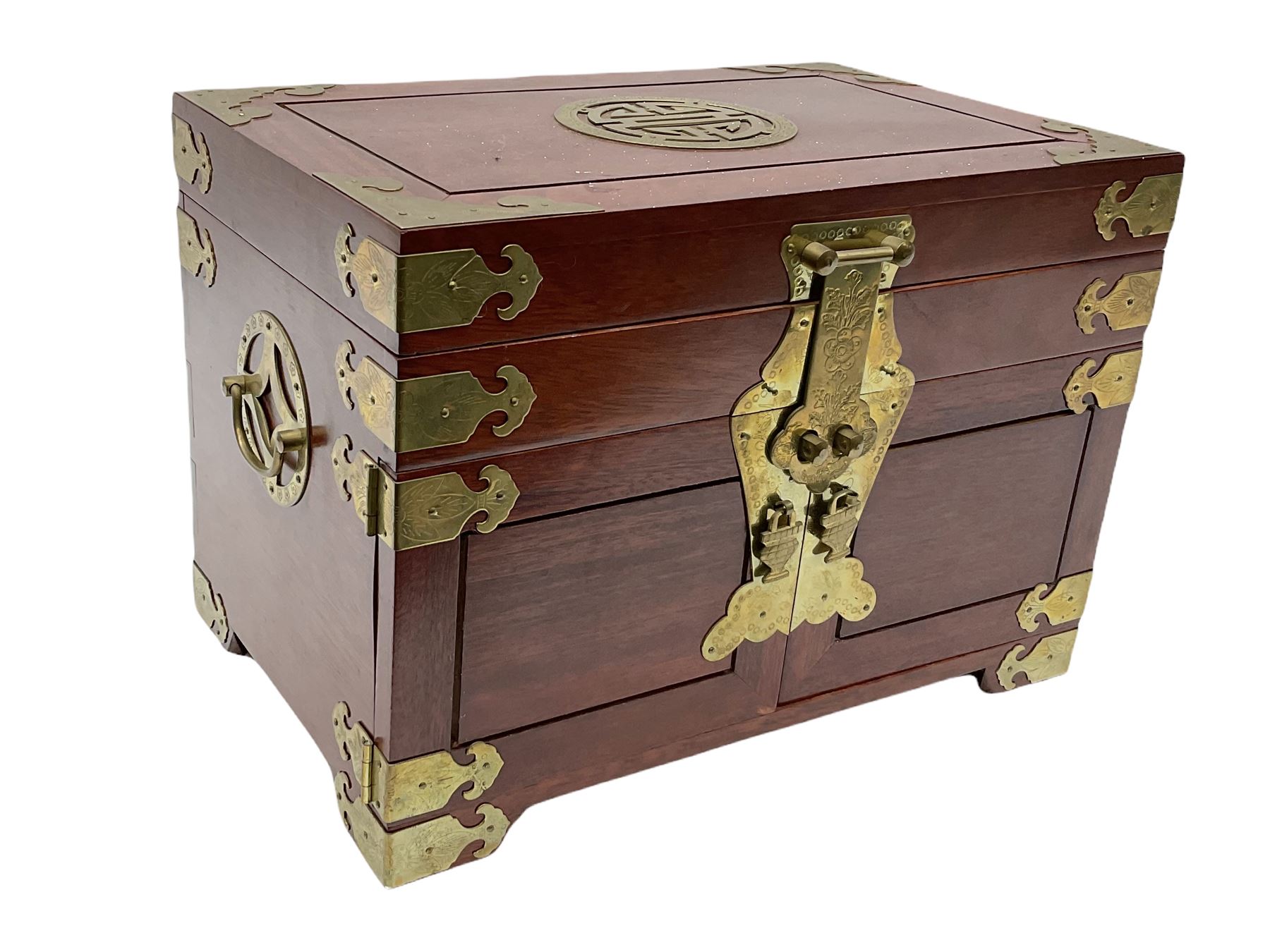 Chinese hardwood jewellery box mounted with engraved brass fixtures, the two exterior doors revealing three drawers below the hinged upper lid, lined with red material decorated with floral sprays, H25cm, W36cm, D23cm