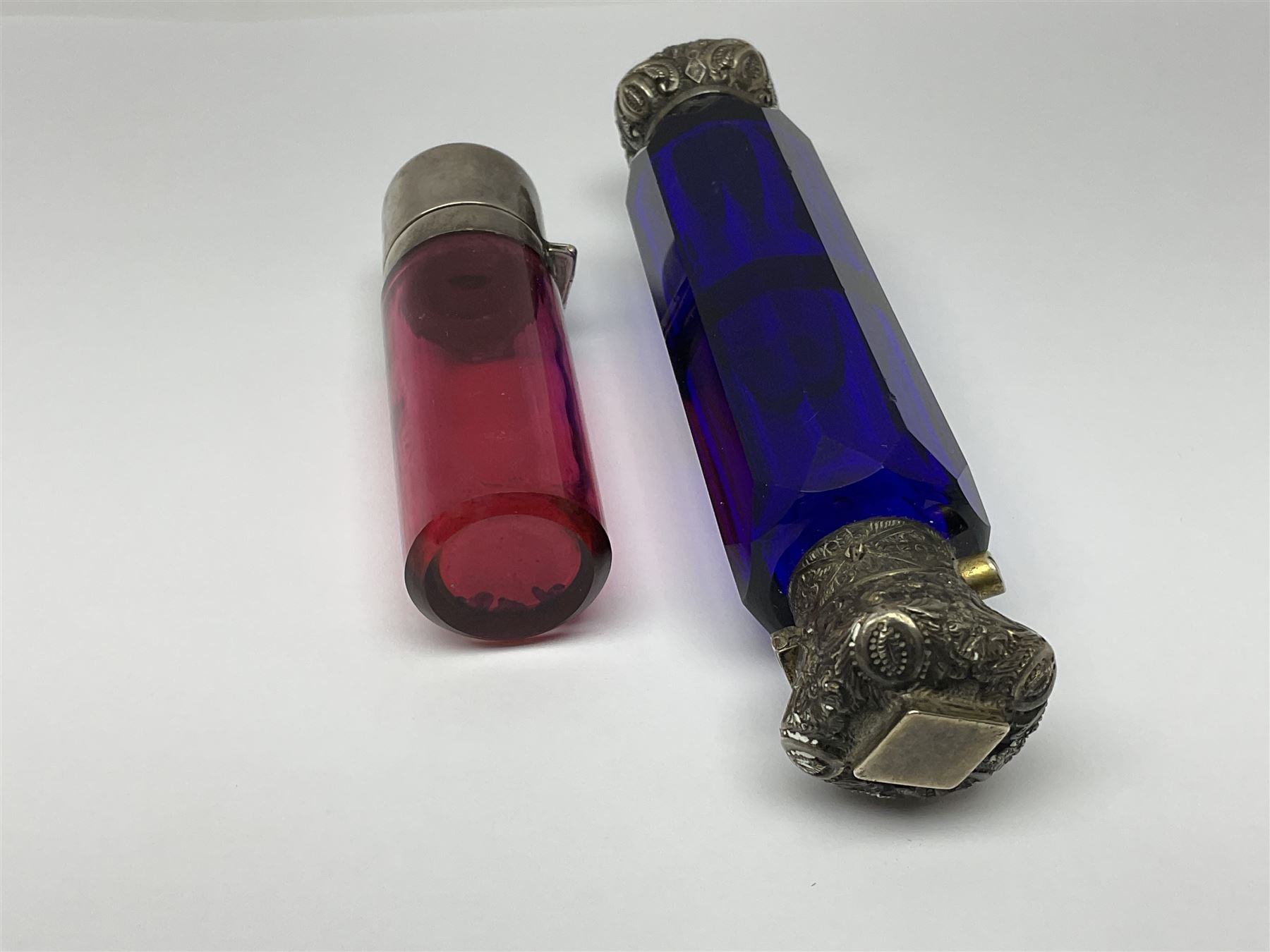 Late Victorian silver mounted ruby glass cylindrical scent bottle, with interior glass stopper, Birmingham 1900, makers mark worn, H8cm, together with a Victorian double ended cut blue glass perfume bottle mounted with white metal screw and flip caps decorated with foliate repousse detailing, H13.5cm