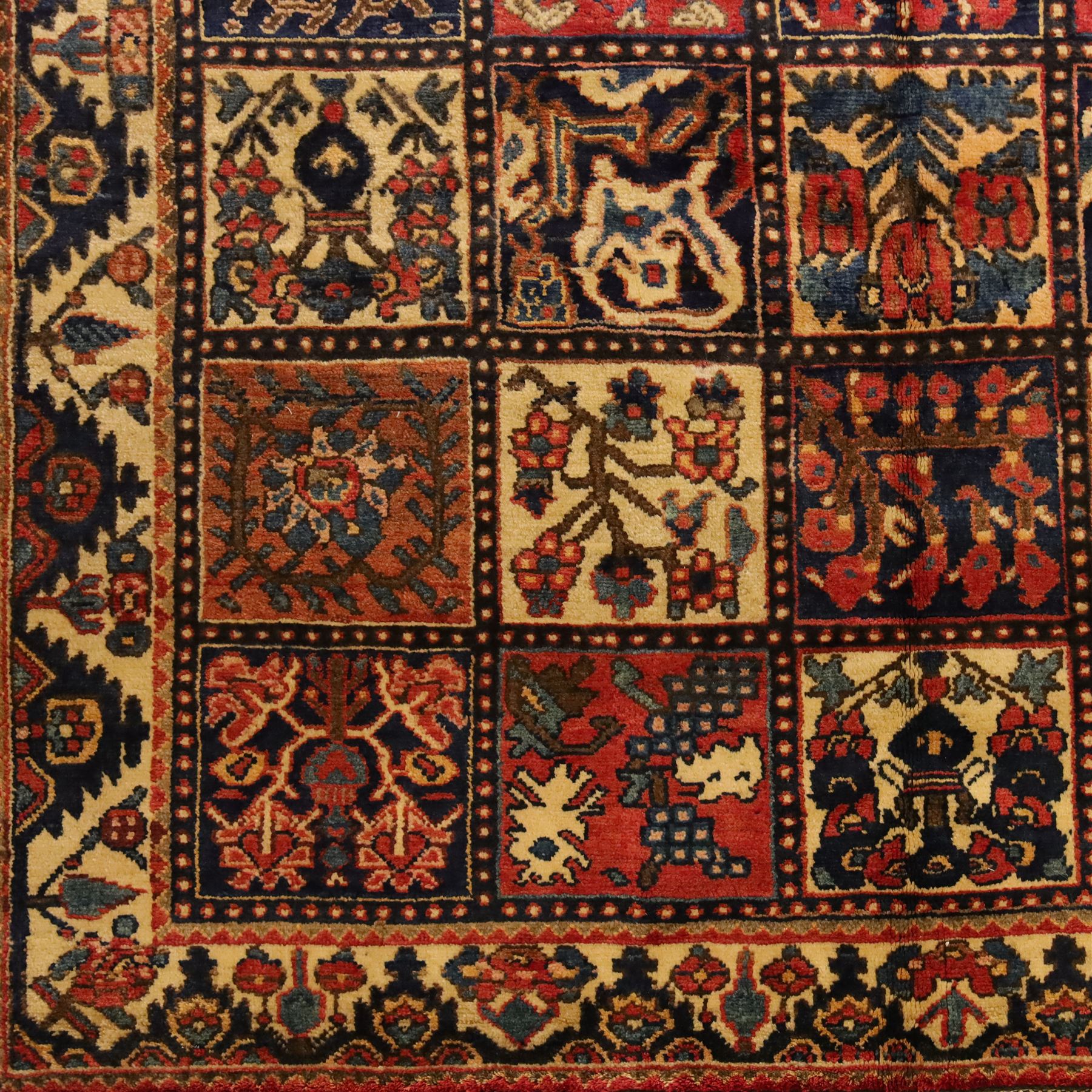 Central Persian Bakhtiari Kheshti design hand-knotted rug, field composed of a grid of square panels, each containing stylized floral devices, animal and foliate motifs woven in a rich palette of madder red, indigo blue, ivory ochre and brown, framed by a multiple striped border with a meandering vine and flowerhead band, with cotton fringe ends 