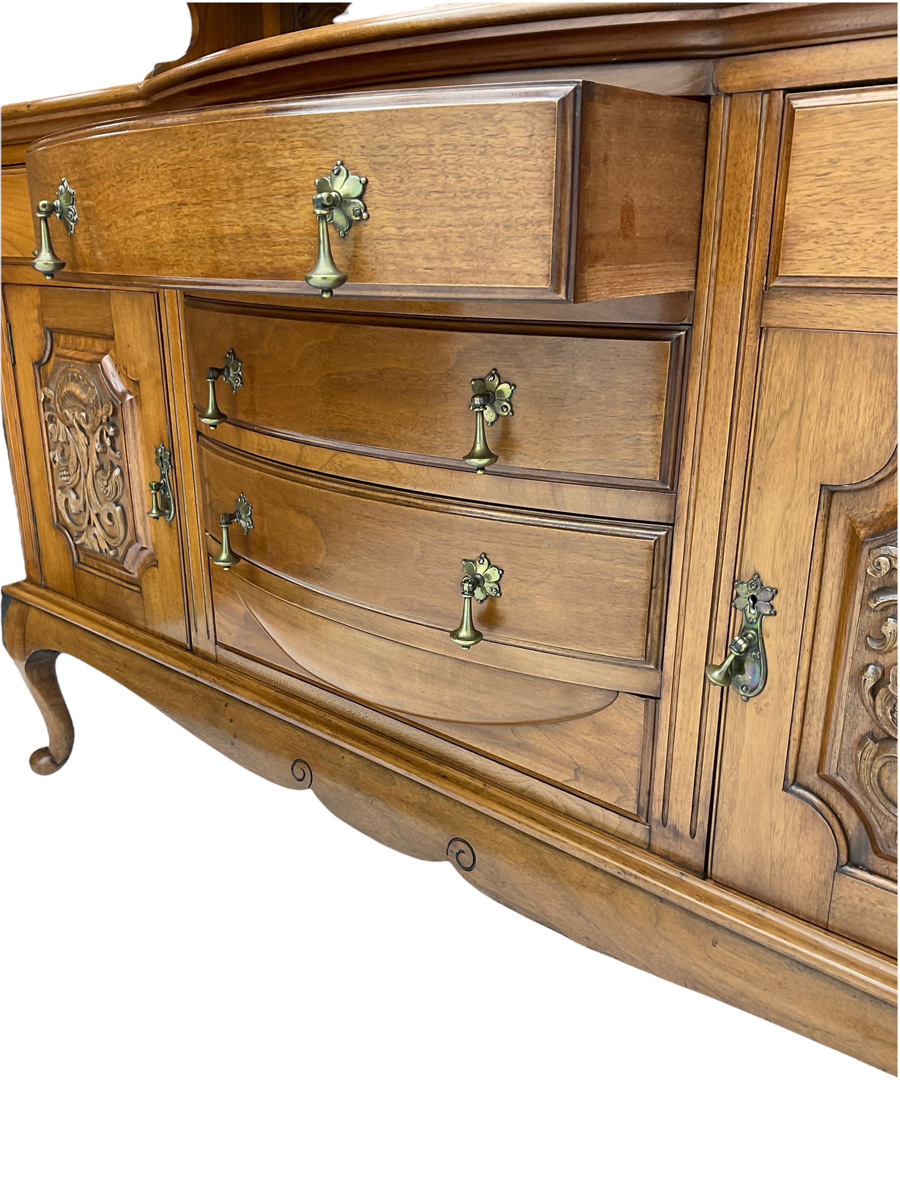 Late Victorian walnut mirror back sideboard or dresser, the raised back fitted with two curved and lead glazed cabinets, central arched bevelled mirror, the sideboard with break bowfront, fitted with six drawers and two cupboards, the cupboard doors panelled and carved with scrolls, shell and plant motifs, shaped apron with cabriole feet
