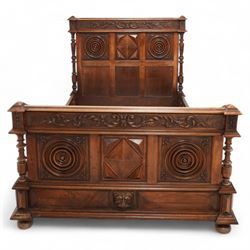 Late 19th century French walnut double bedstead, the panelled headboard with curling foliage carved frieze over concentric turned roundels and faceted mounts, lion mask carved rails with applied panelled mounts, matching footboard with lower carved lion mask 