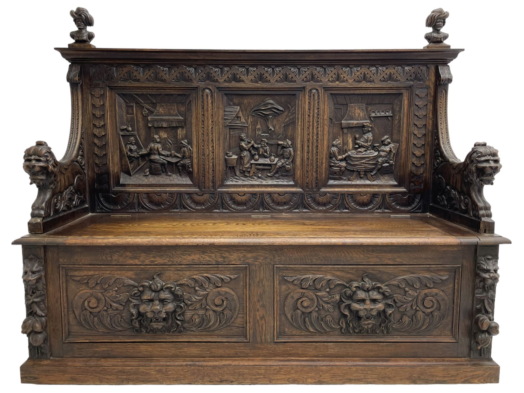19th century heavily carved oak settle, the moulded upper rail over triangular foliage carved frieze, three Flemish style carved panels depicting tavern scenes, acanthus carved uprights terminating to lion carved arms, hinged box seat, the panelled front carved with lion masks and extending scrolled acanthus leaves, on moulded skirt base