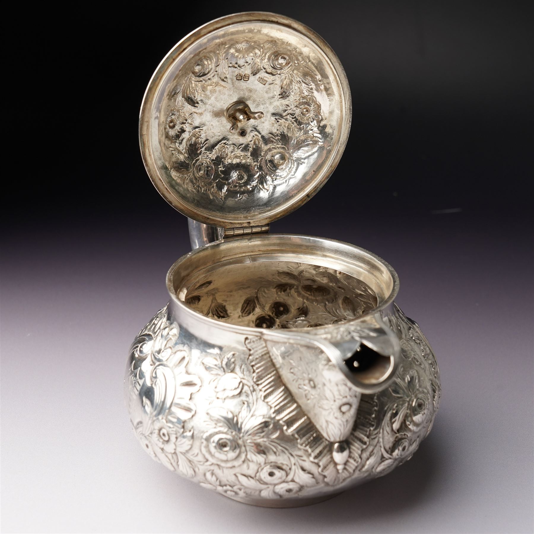 Matched three piece silver tea set comprising teapot of squat circular form London 1827,  milk jug of similar date and sugar bowl with Britannia standard marks, all with later embossed floral decoration and coat of arms, all marks rubbed