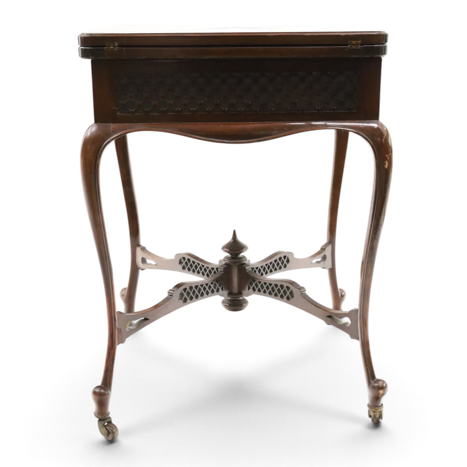 Edwardian carved mahogany envelope card table, the rectangular quadruple hinged top enclosing baize-lined interior, the single frieze drawer and sides with blind-fretwork carving, over cabriole supports with scroll feet and castors united by pierced lattice fretwork X-stretcher with turned finial