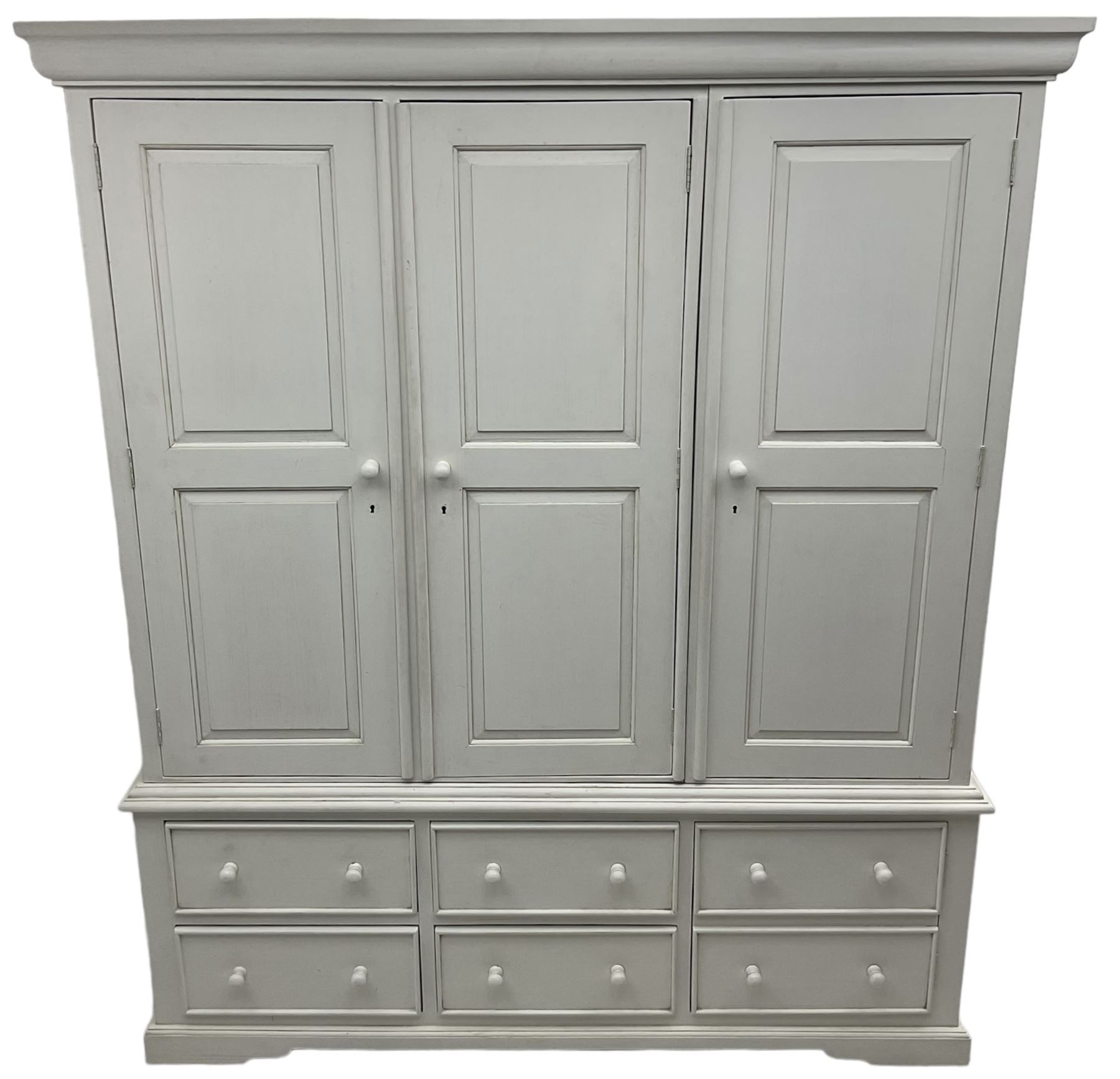 White painted triple wardrobe, projecting moulded cornice over three panelled doors, the interior fitted with hanging rails, four drawers and hinged cupboard to base, on bracket feet