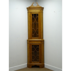  Graduated pair of 20th century golden oak standing corner cabinets, swan neck pediments and astragal glazed doors, on shaped aprons and bracket feet, H208cm, W57cm & 77cm, D31cm & 41cm, (2)   