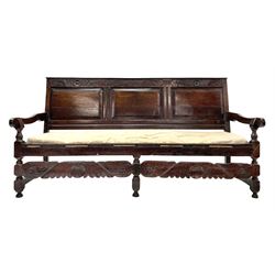 Early 18th century carved oak settle, top rail relief carved with foliage scrolls and flower heads, initialled 'K.W.I' and dated '1718', triple fielded panel back above strung seat with upholstered squab cushion, turned supports joined by shaped shell and foliate carved rails