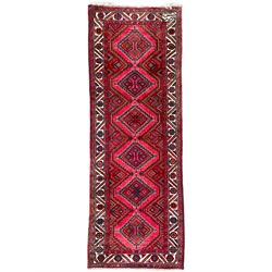 Persian Hamadan red ground rug, decorated with six stepped lozenge medallions, the guarded border with repeating stylised flower head decoration, with inscription to corner