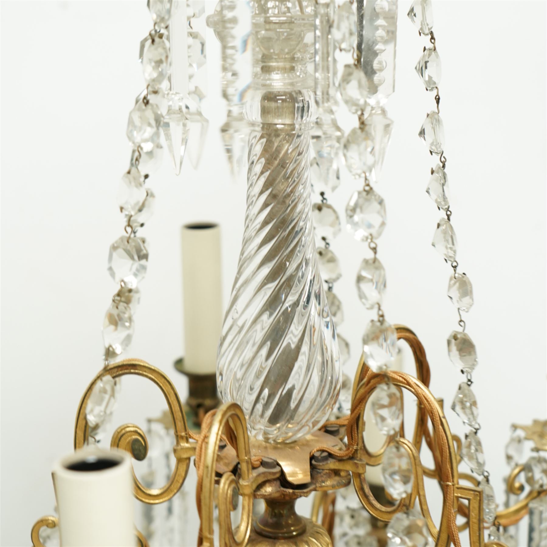 Late Victorian gilt bronze mounted crystal chandelier, ceiling rose above shaped top of trailing swags, glass crystal droplets, beneath rising curled branches and glass beads tapering down to five candle sconces, inside circular bezel fitted with drops and glass twist fluted stem, supported with an internal metal shaft above a rococo style stem holding double branches, and similar styled branches, with twelve branches fitted with candle holders and drip trays with crystal drops and cut crystal spears, the underside festooned with crystal glass swags and a bulbous fluted glass terminal and shaped finial with crystal glass swags attached to the branches, the base with pear shaped droplet graduating to the centre, wired for electricity 