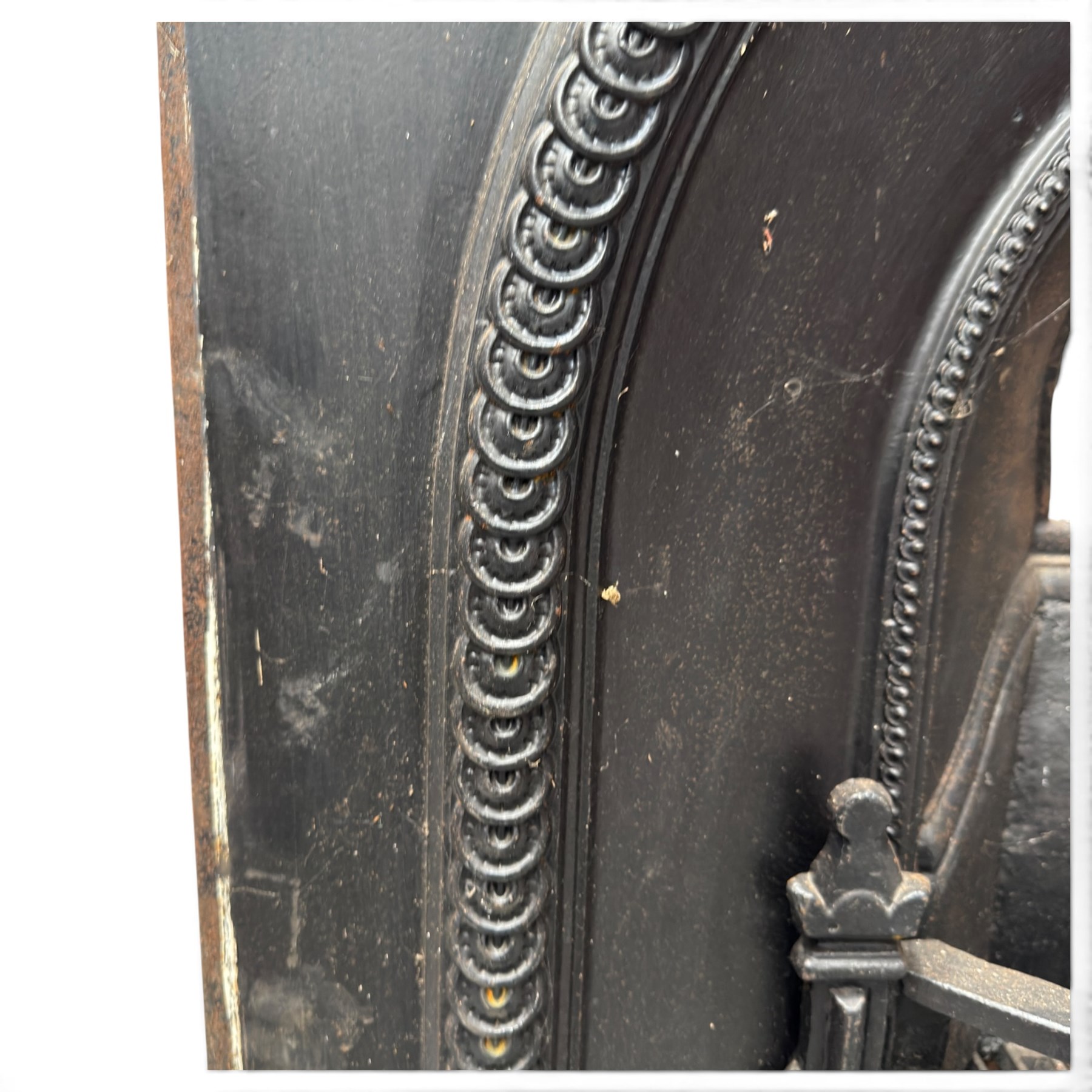Late Victorian black-painted cast iron fireplace, the arched surround with anthemion cartouche and guilloche-moulded border, enclosing a bow-front fire basket with finialled standards, railed front and leaf-cast apron, with sheet-metal backplate